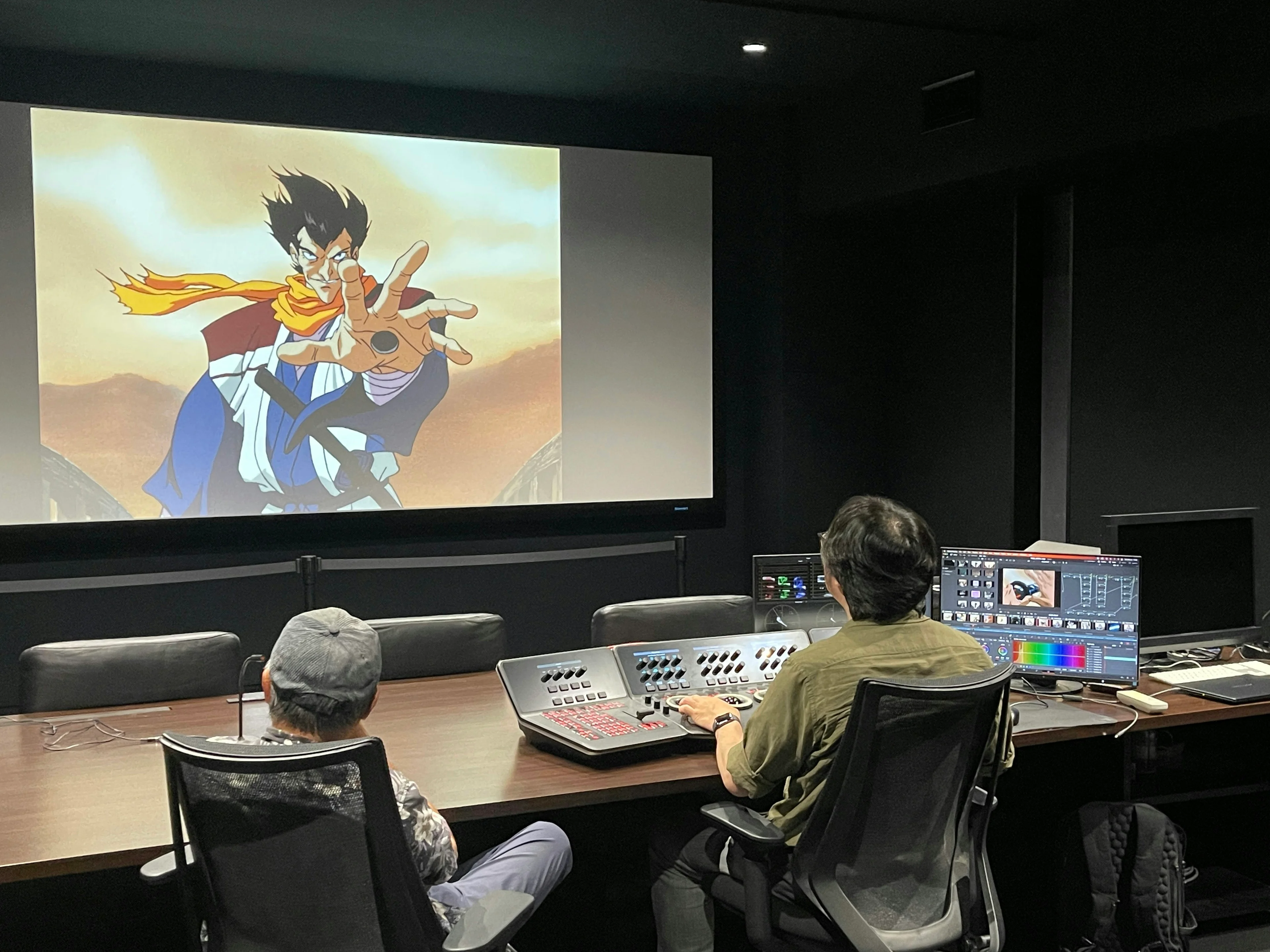 The restoration team reviews an animated character on a large screen beside monitors and color controls.