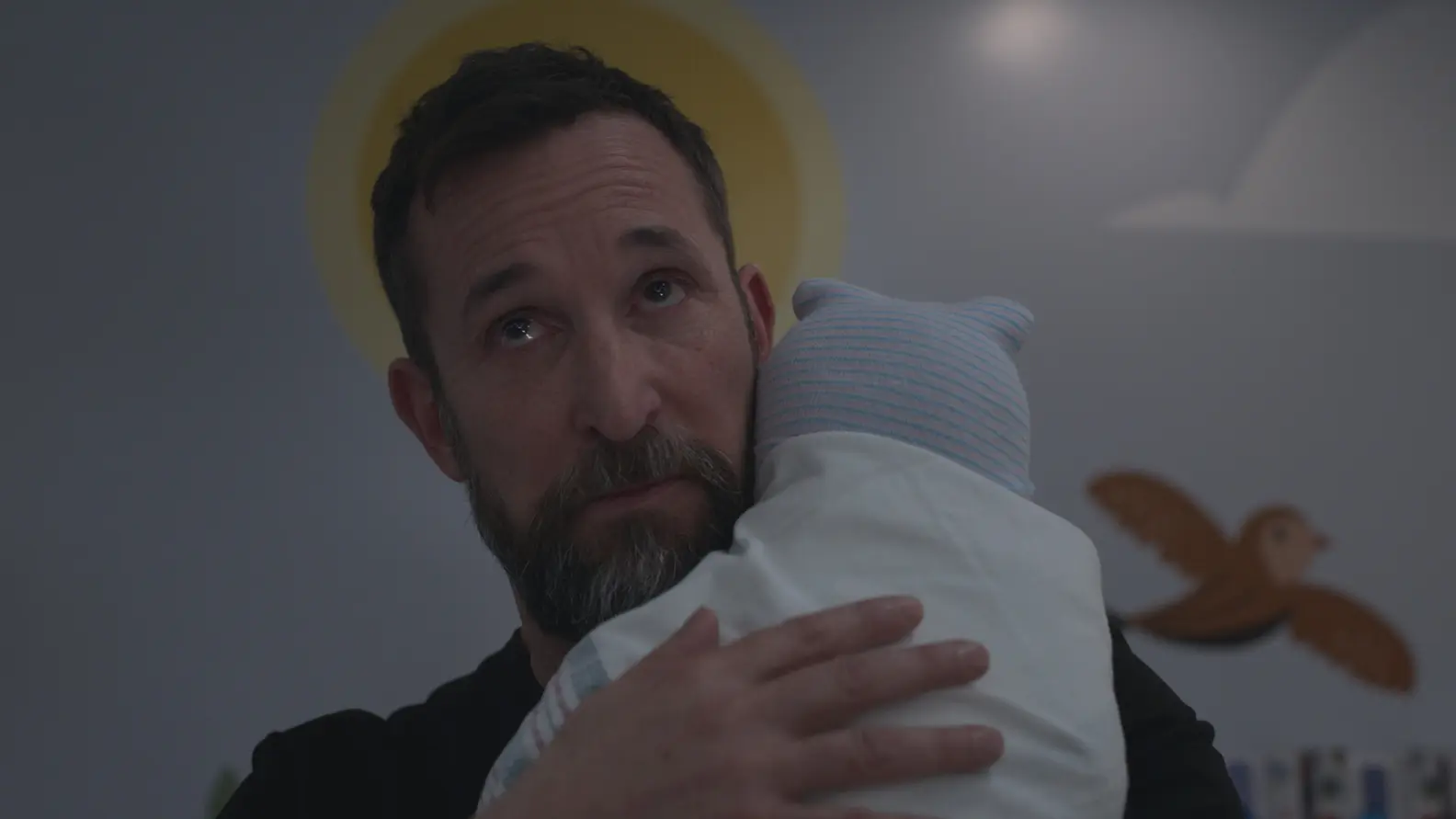 Noah Wyle as Dr. Robby holds a newborn in The Pitt.