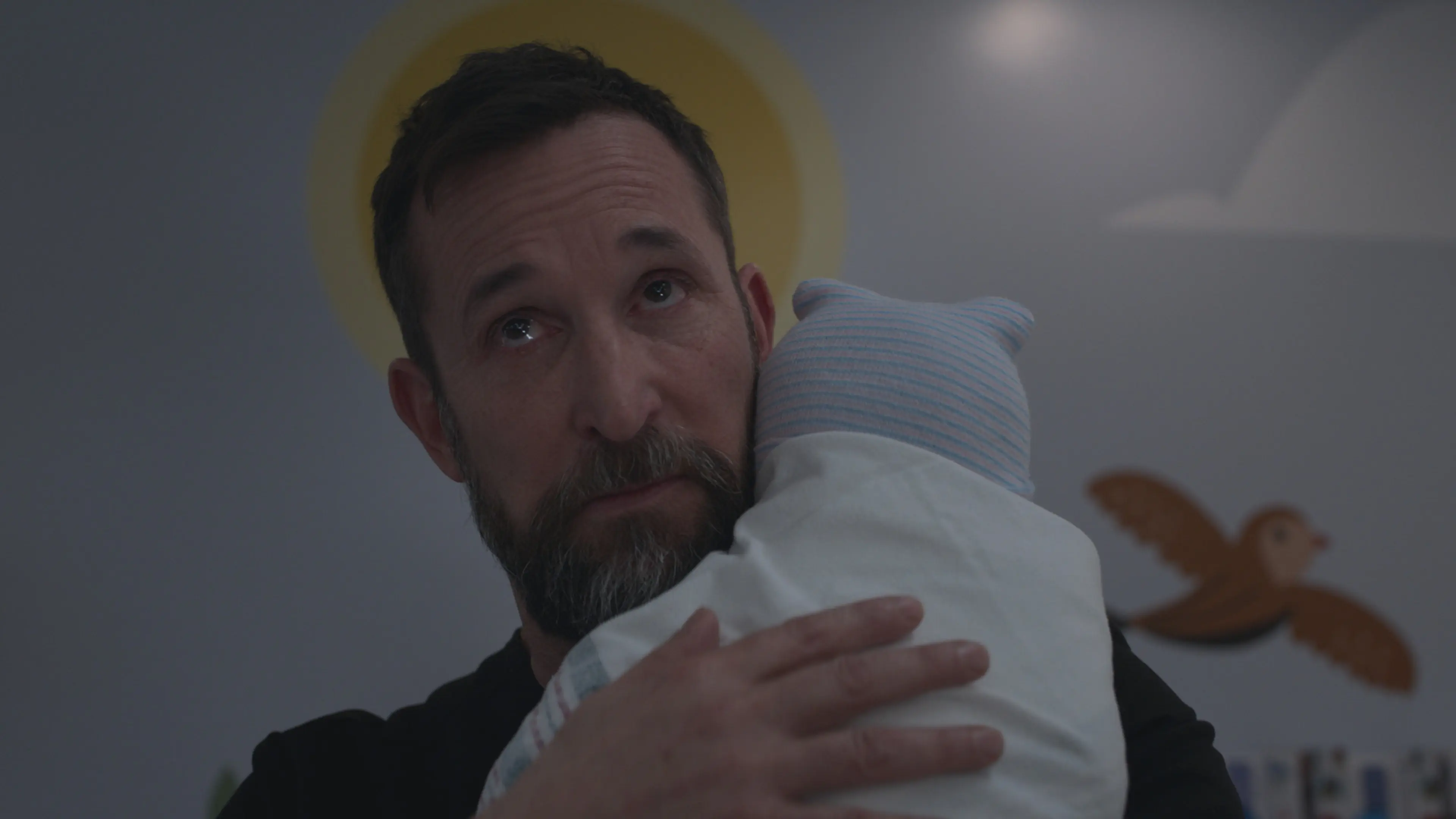 Noah Wyle as Dr. Robby holds a newborn in The Pitt.