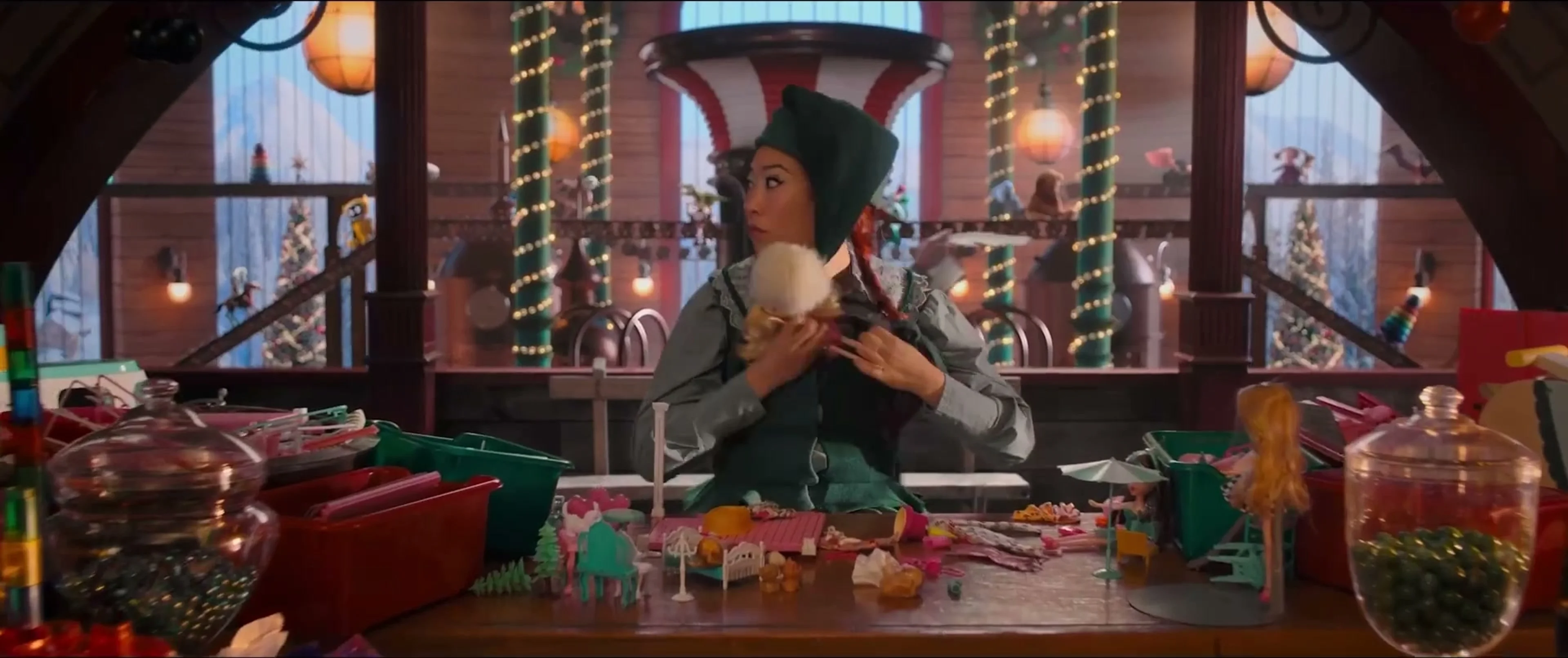 Awkwafina wears an elf costume in a workshop filled with toys.