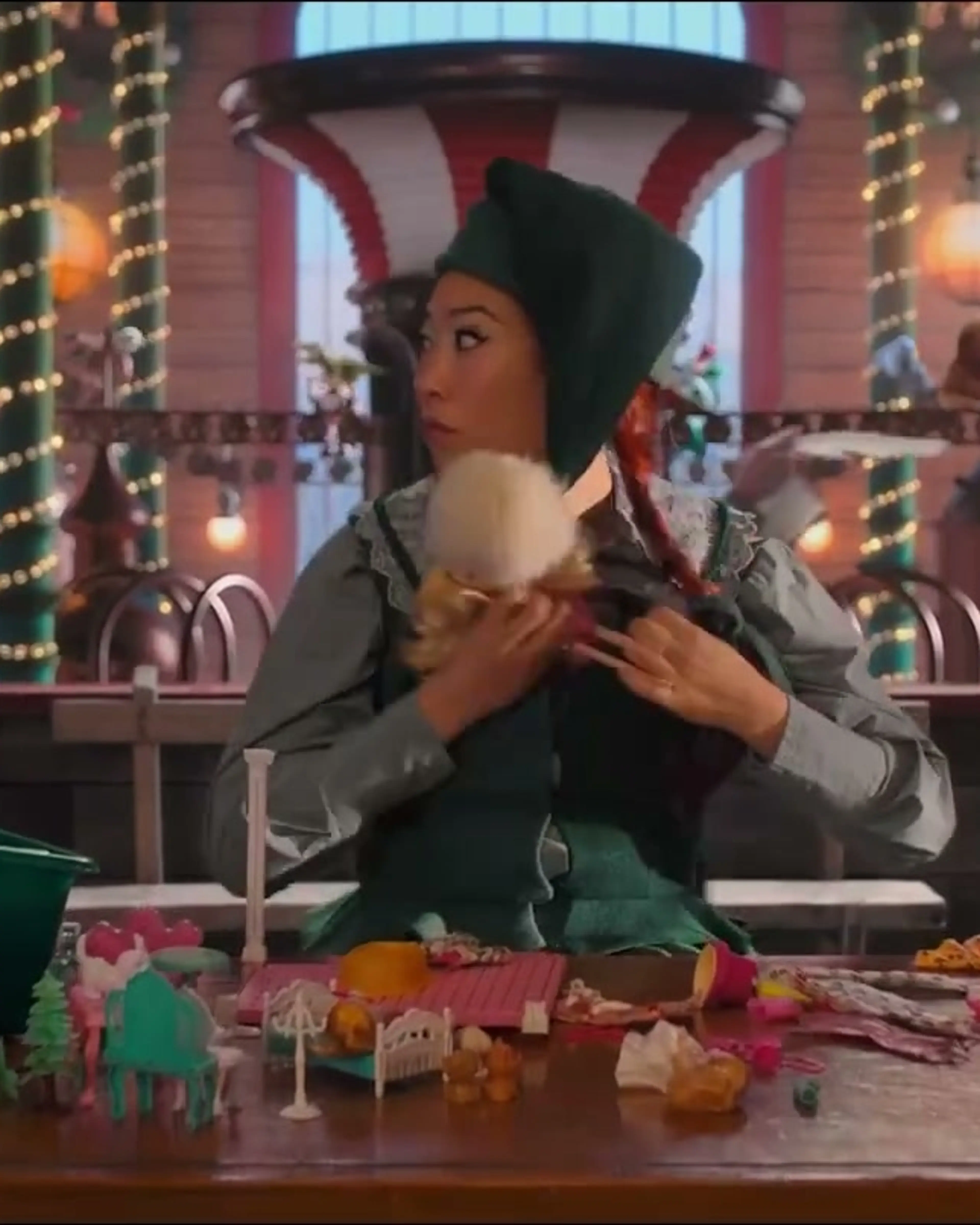 Awkwafina wears an elf costume in a workshop filled with toys.