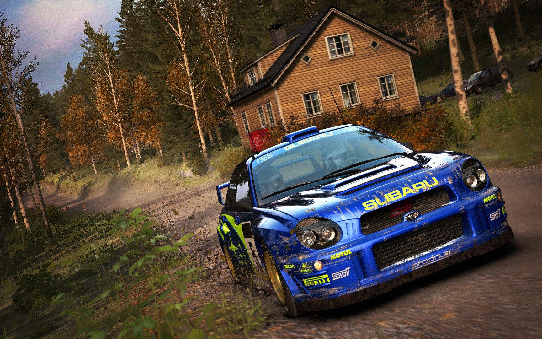 Blue Subaru rally car travels down a narrow forest road beside a wooden building.