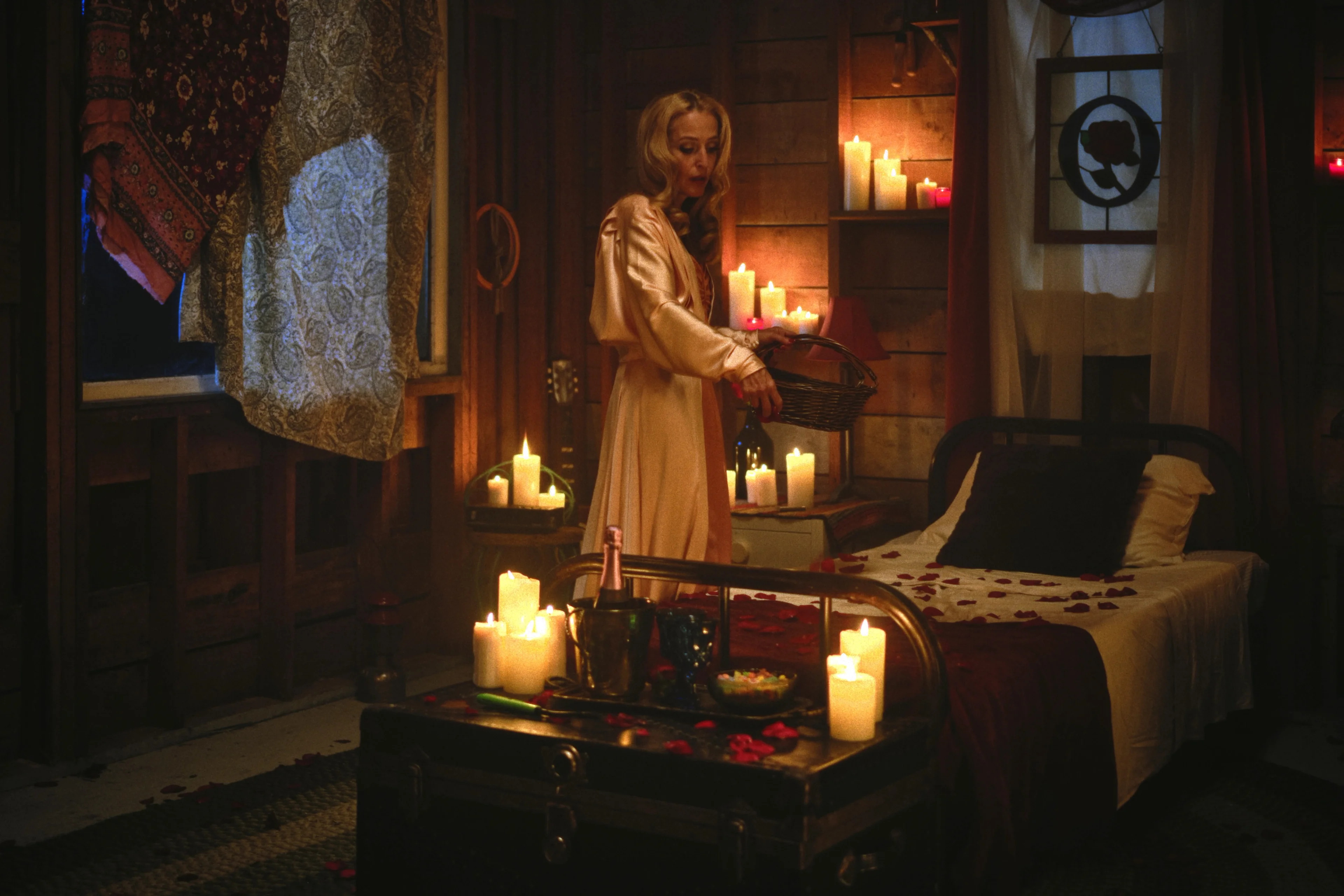 Gillian Anderson as Billy stands in a robe in a candlelit wooden room.