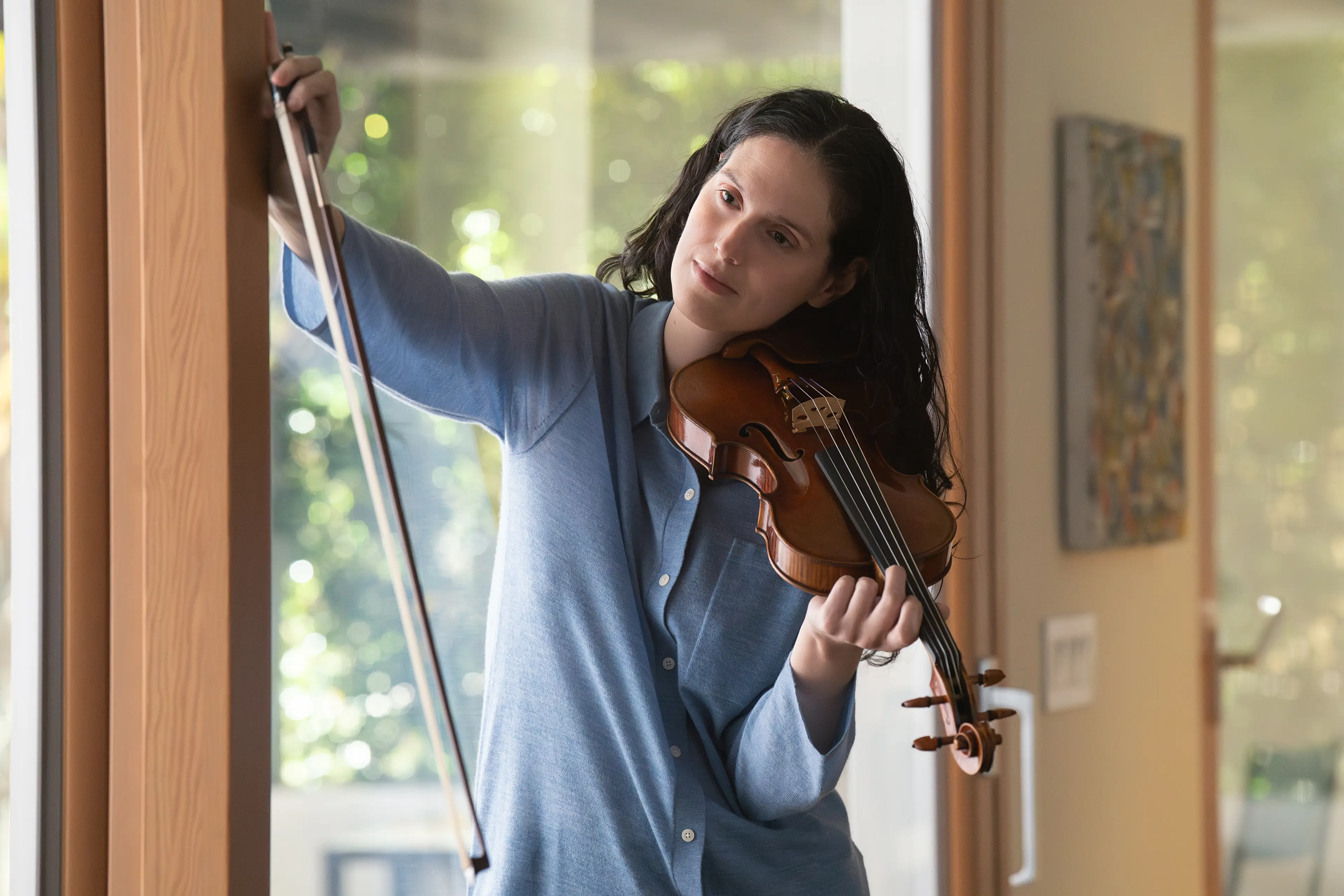 Eva Victor plays a violin beside a window in Behemoth!.
