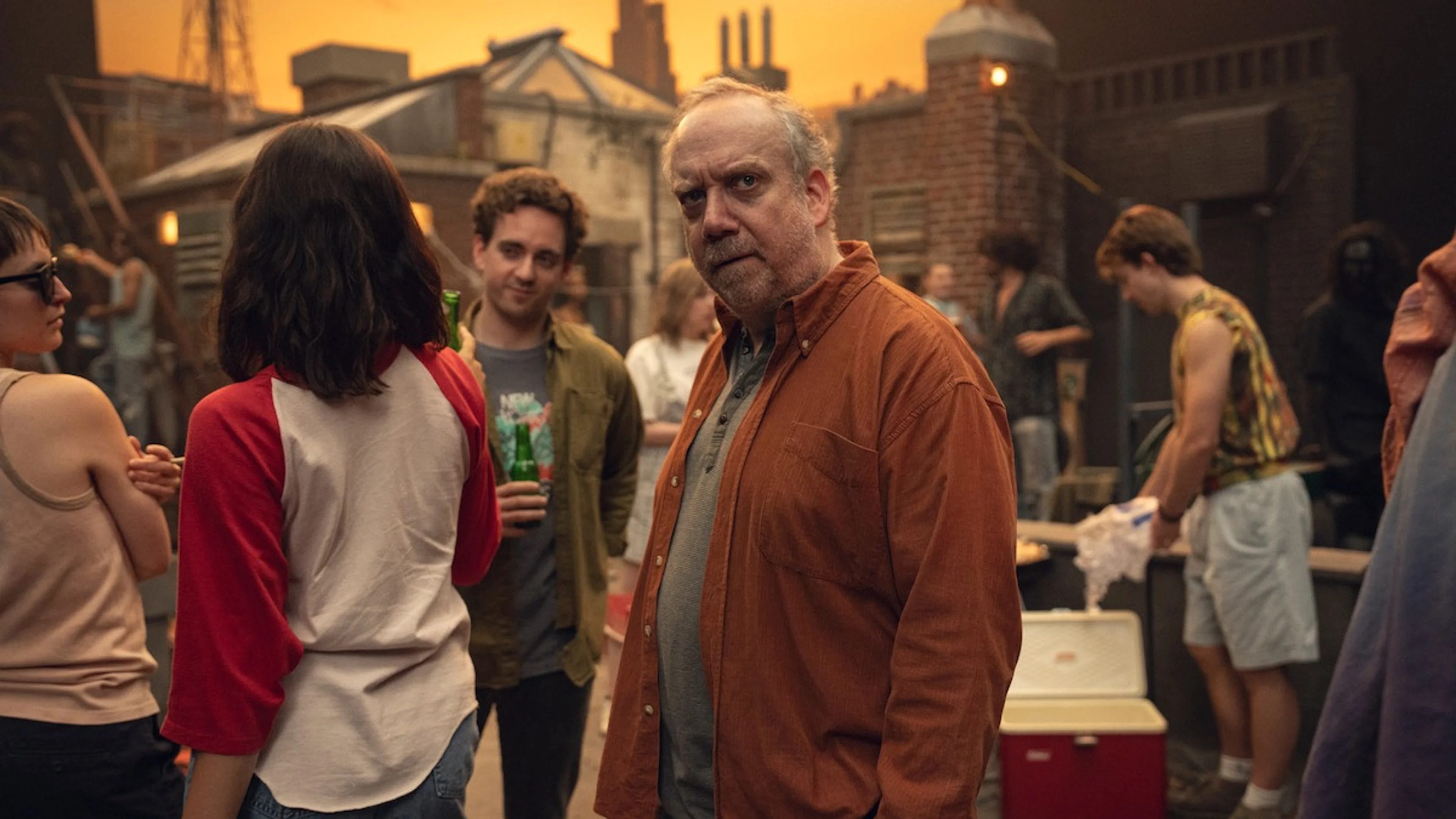 Paul Giamatti looks toward the camera in an official Black Mirror Season 7 still set at an outdoor gathering.