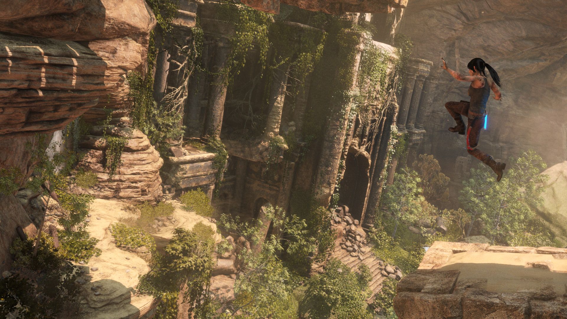 Lara jumps between ruined stone structures surrounded by green cliffs.