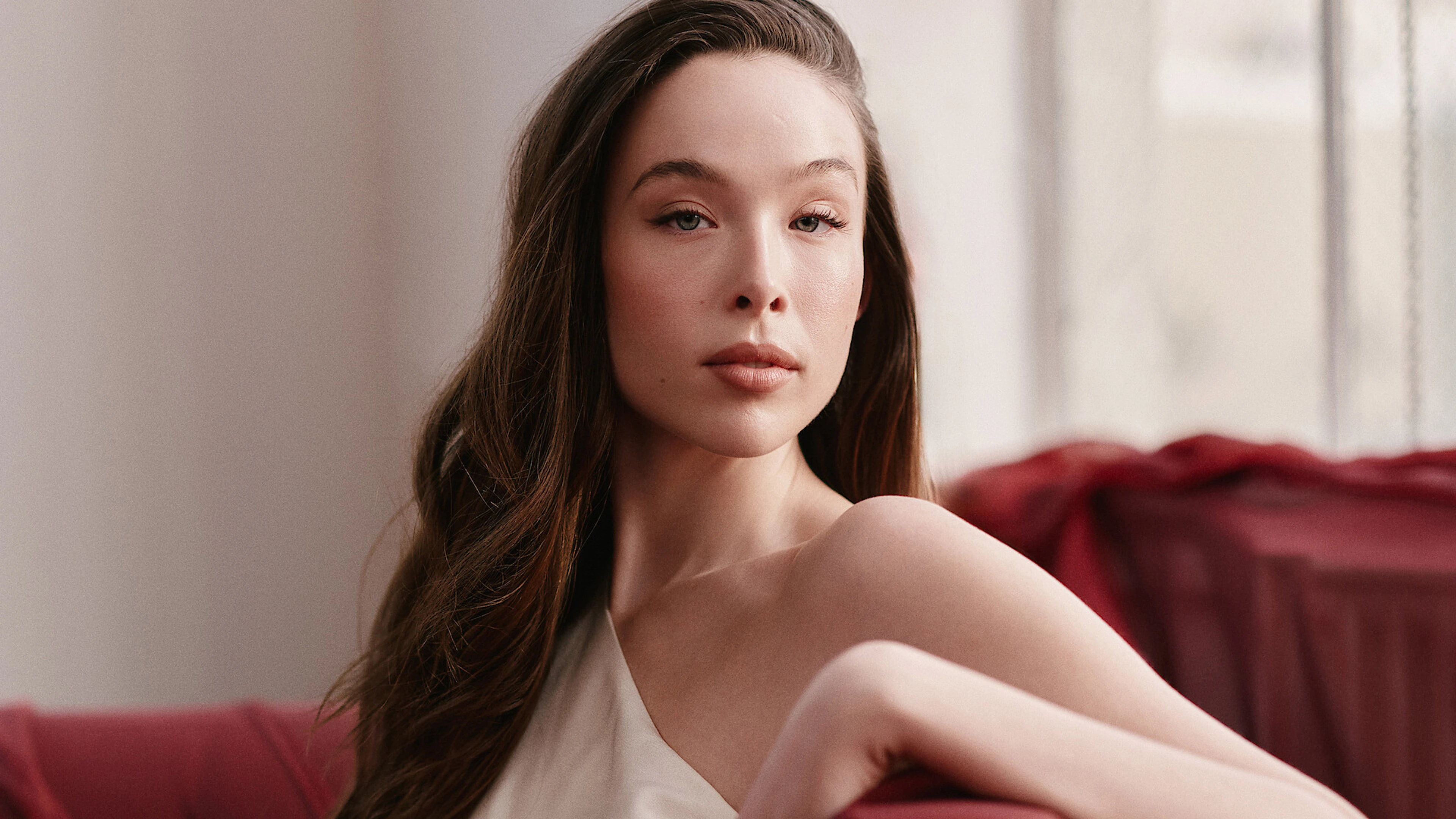 Ella Beatty sits against a red sofa in a crisp editorial portrait.