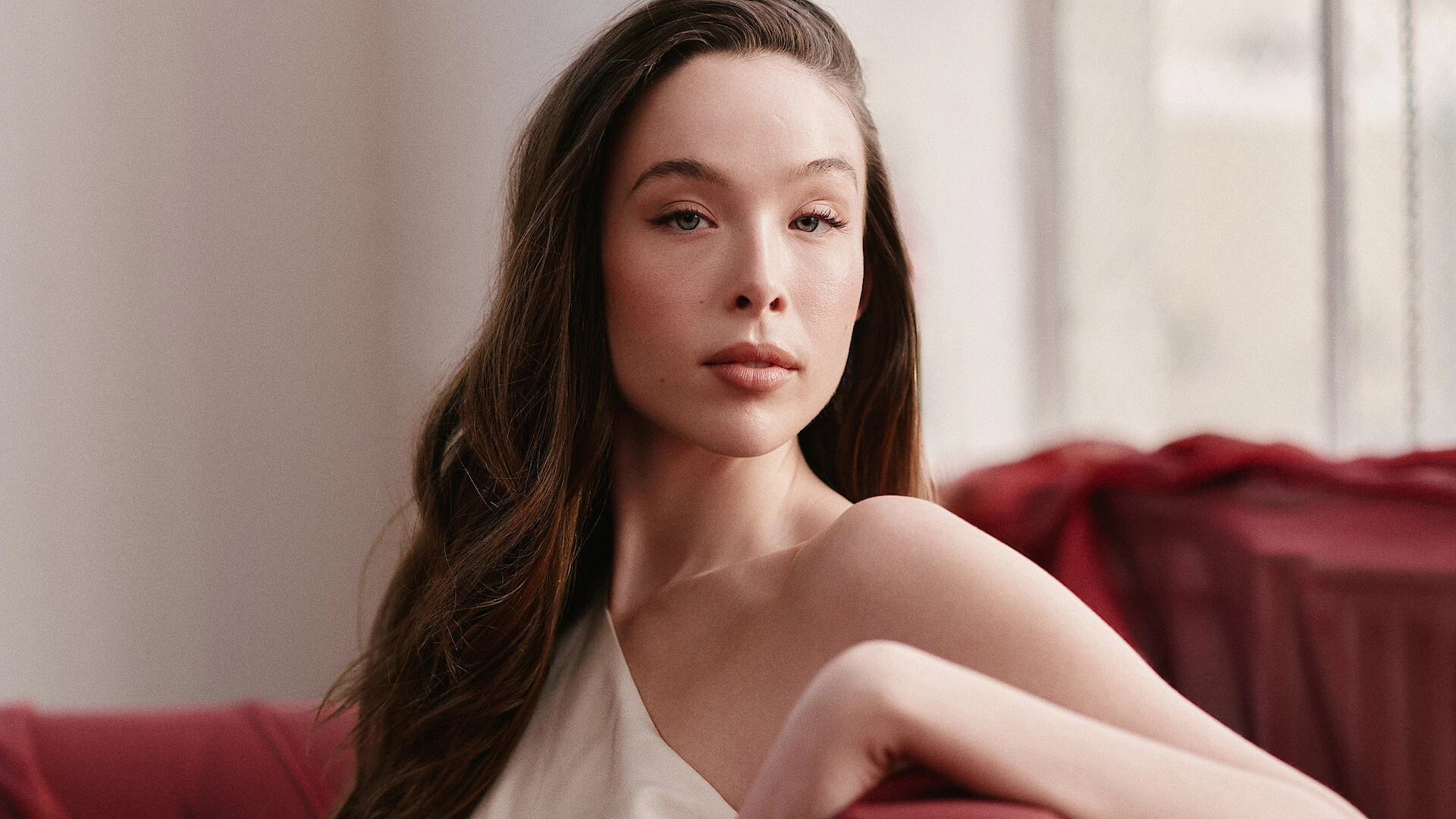 Ella Beatty sits against a red sofa in a crisp editorial portrait.