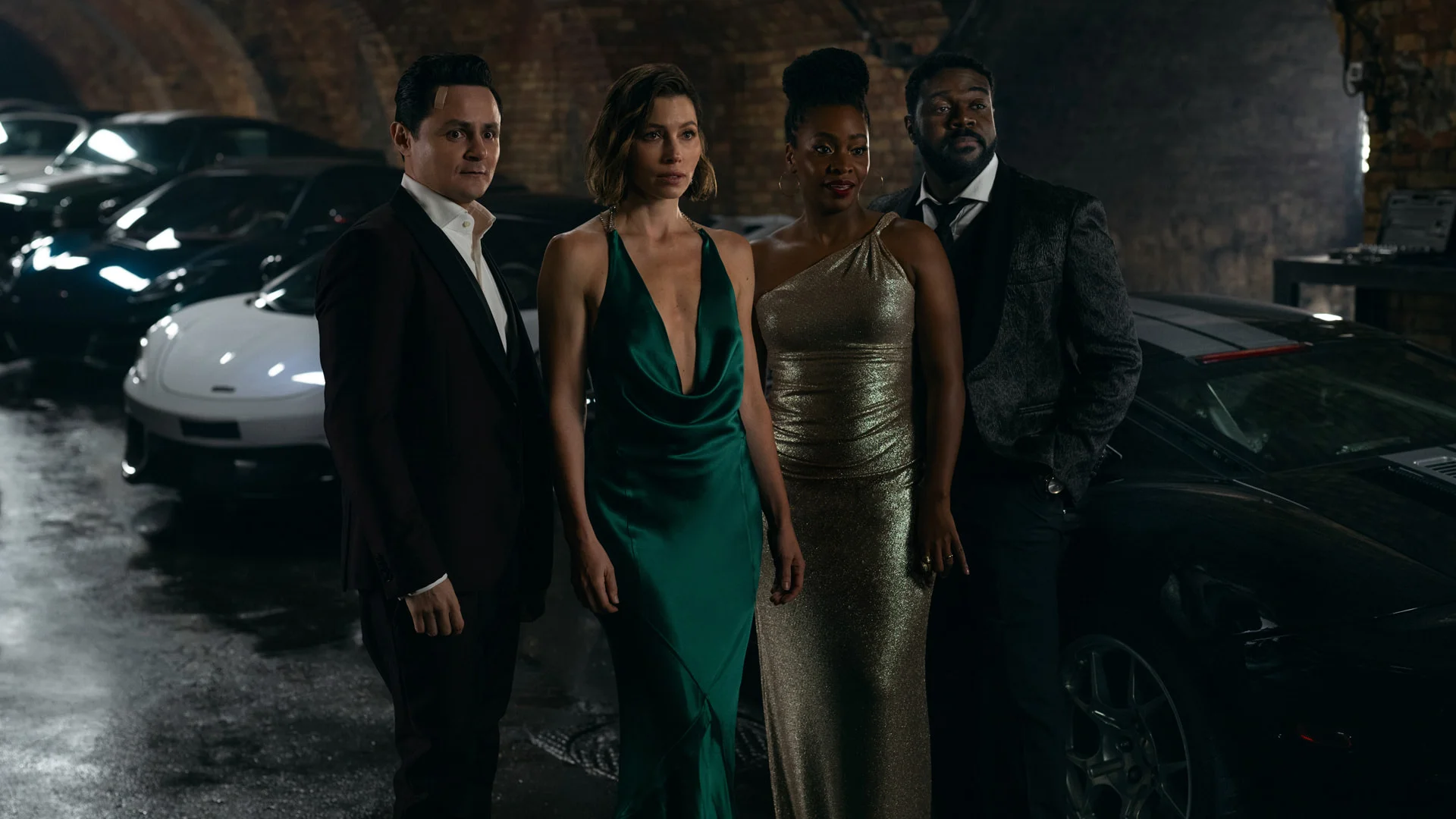 Jessica Biel, Arturo Castro, Teyonah Parris and Sam Richardson stand beside cars in a Matchbox film scene.
