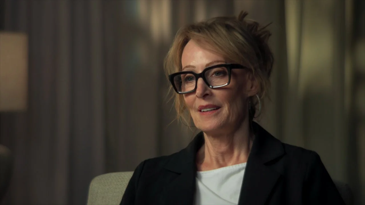 A woman with short hair and glasses speaks during an interview in The Swan: Behind the Mirror.
