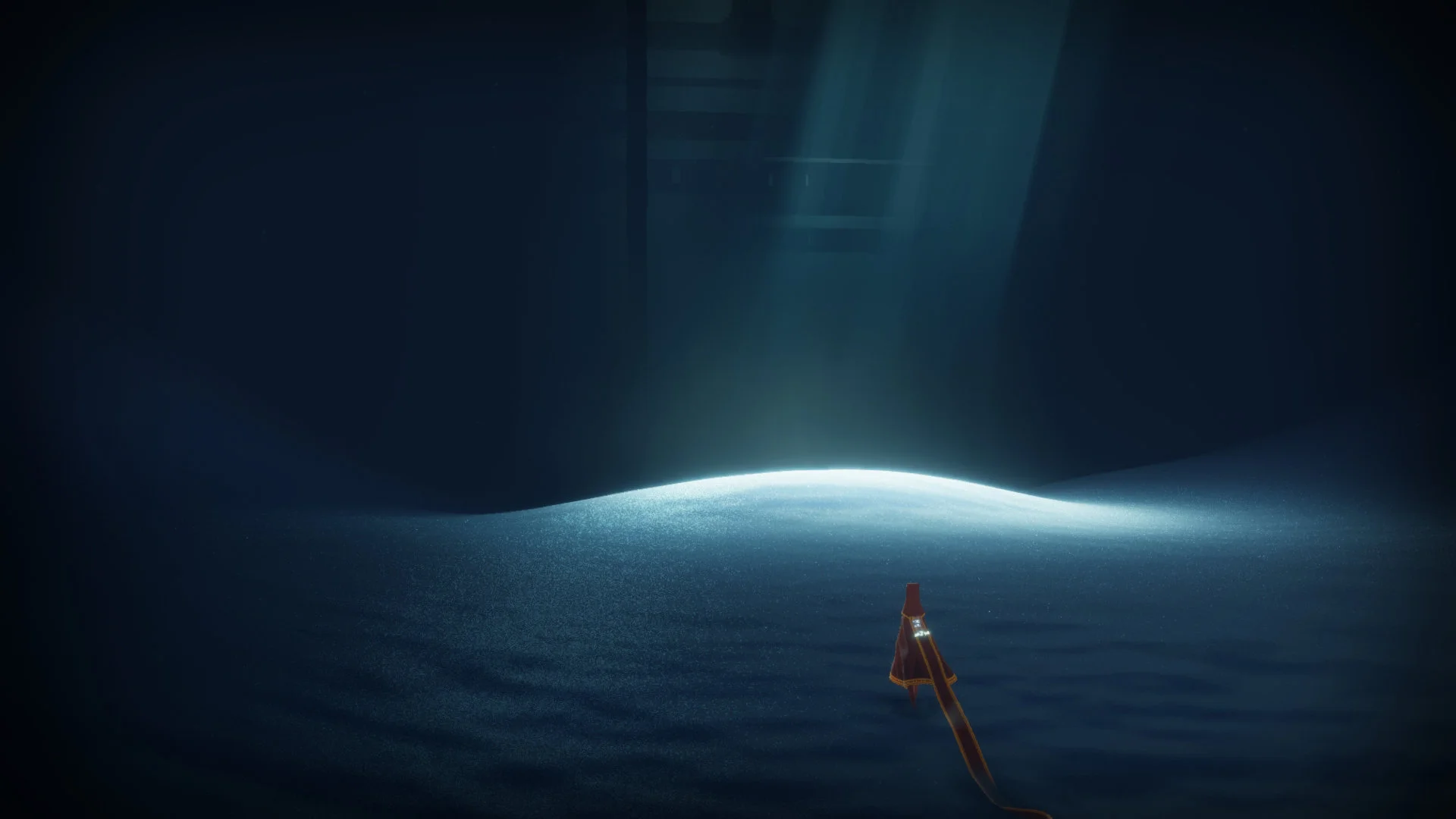 A robed traveler approaches a lit patch of sand in a dark chamber in Journey.
