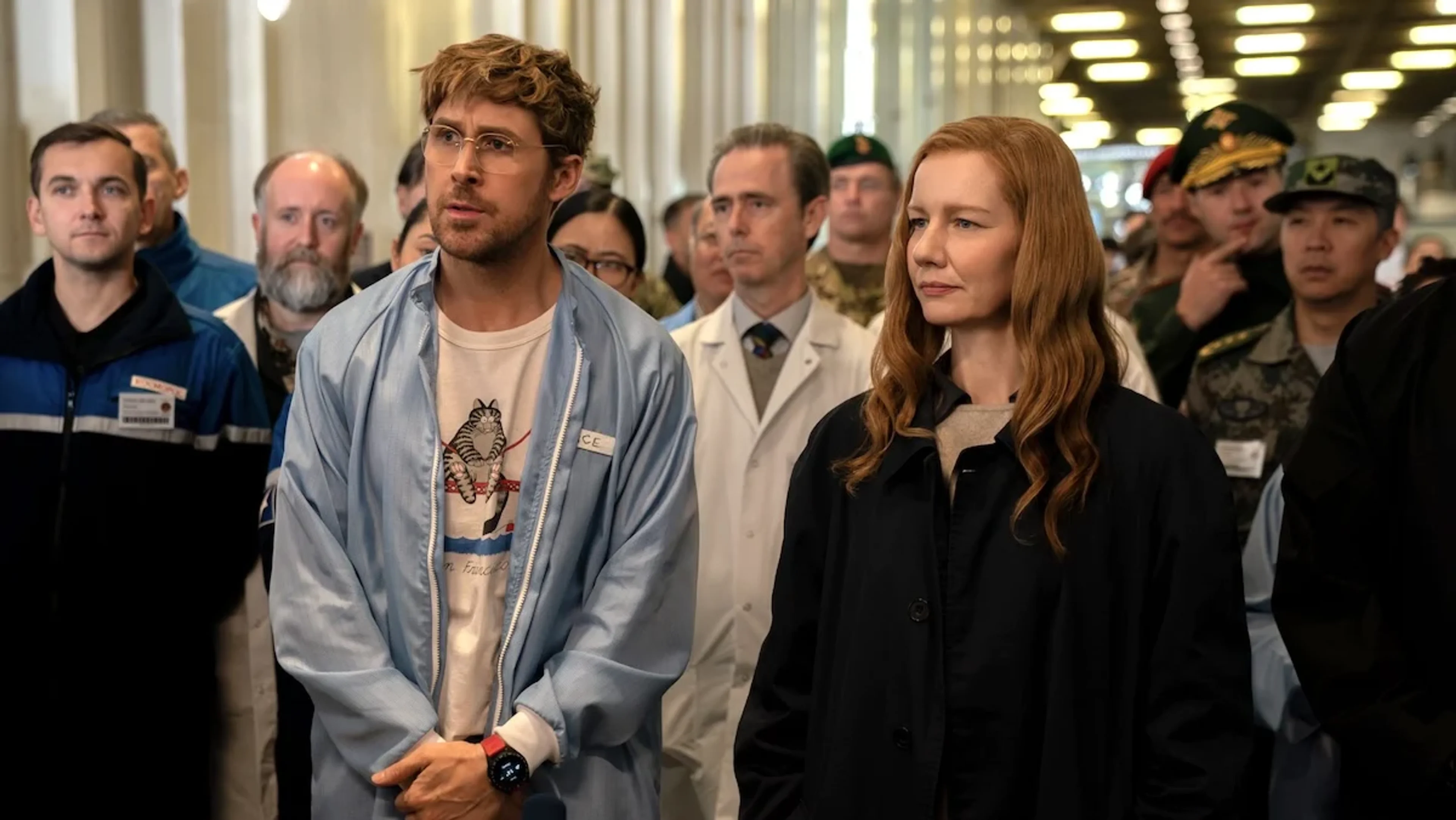 Ryland Grace and Eva Stratt stand in front of a group of scientists and uniformed personnel.