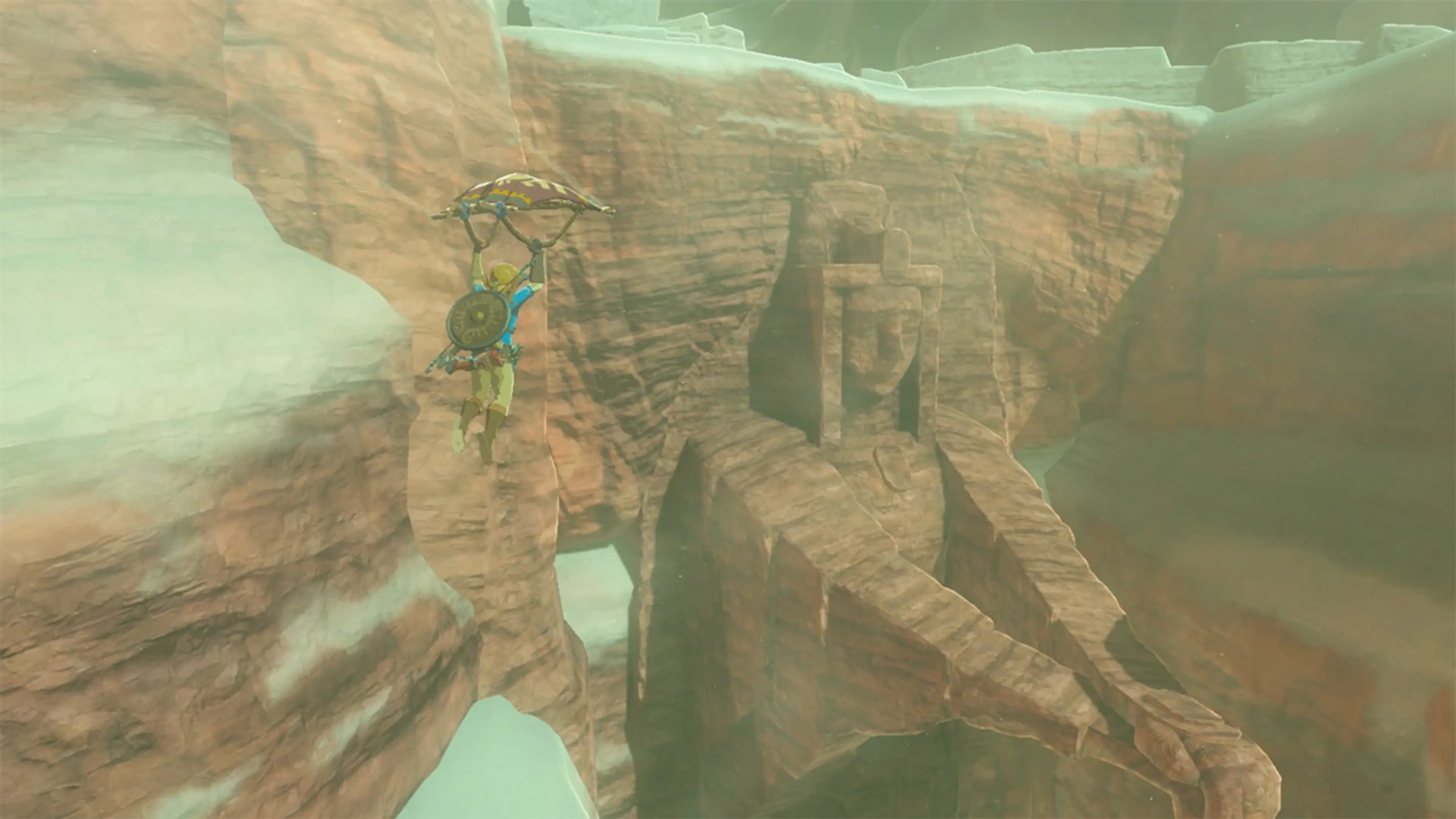 Link uses the paraglider above a desert canyon in Breath of the Wild.