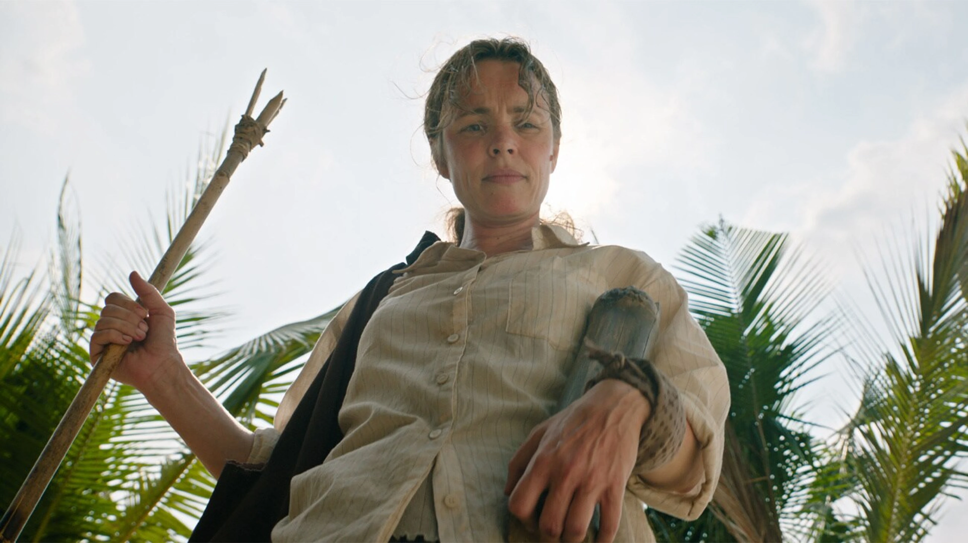 Linda holds a wooden spear under palm leaves in Send Help.