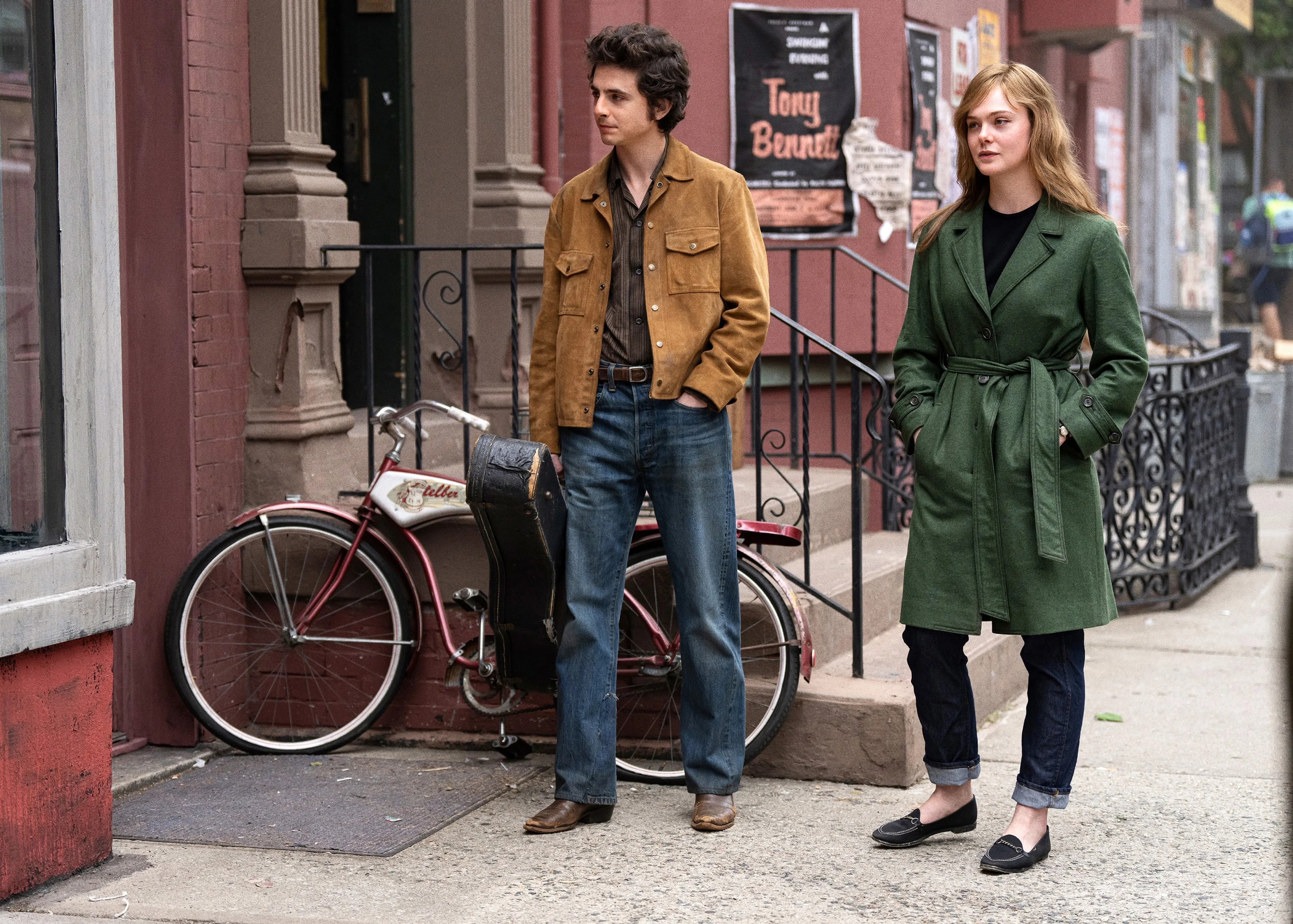 Timothée Chalamet in a tan jacket and Elle Fanning in a green coat walk along a city sidewalk.