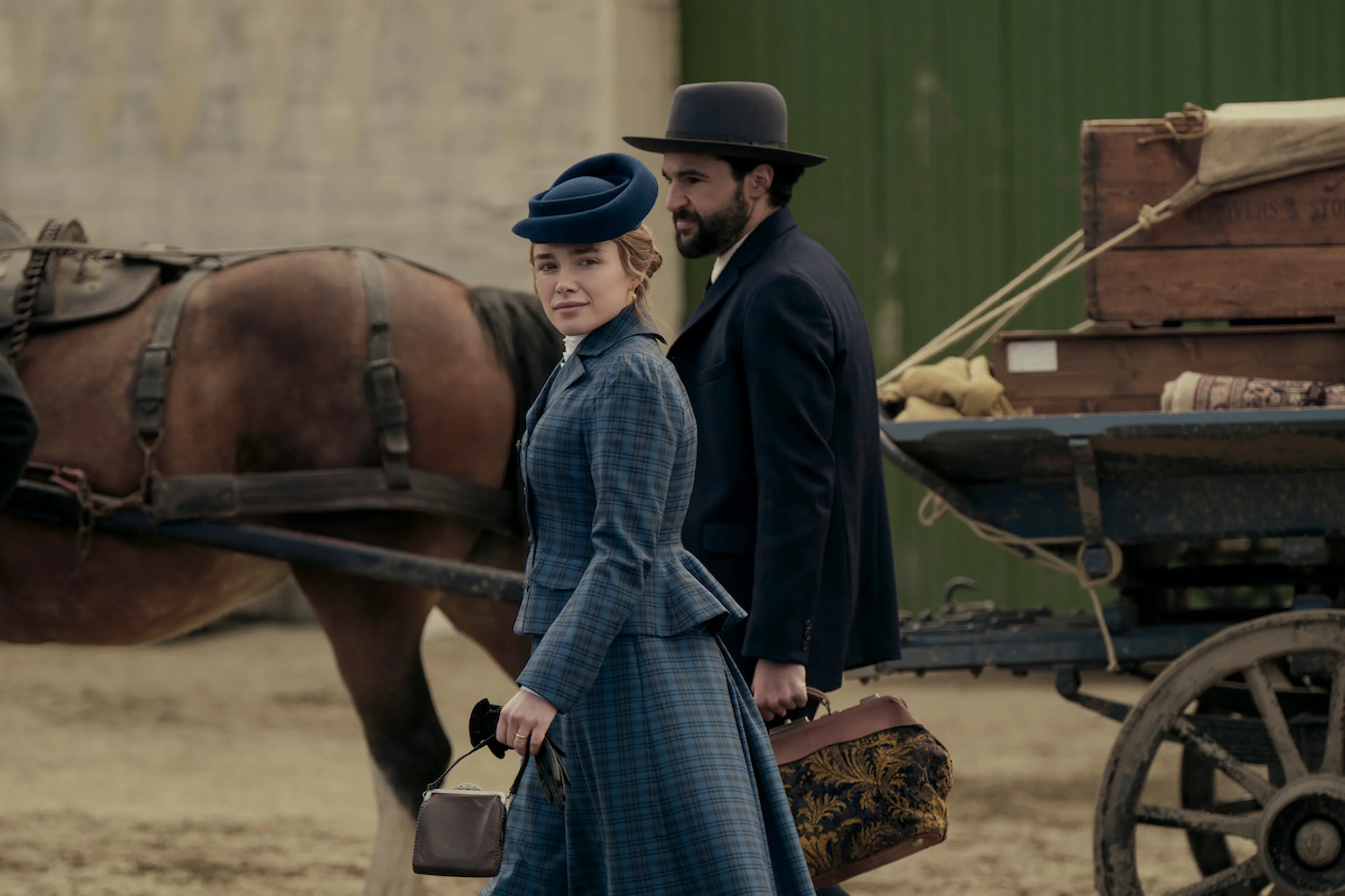 A woman in a blue period dress and a bearded man walk beside a loaded horse-drawn wagon in East of Eden.