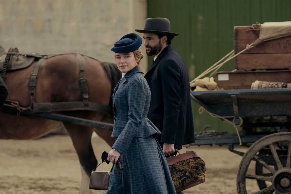 A woman in a blue period dress and a bearded man walk beside a loaded horse-drawn wagon in East of Eden.