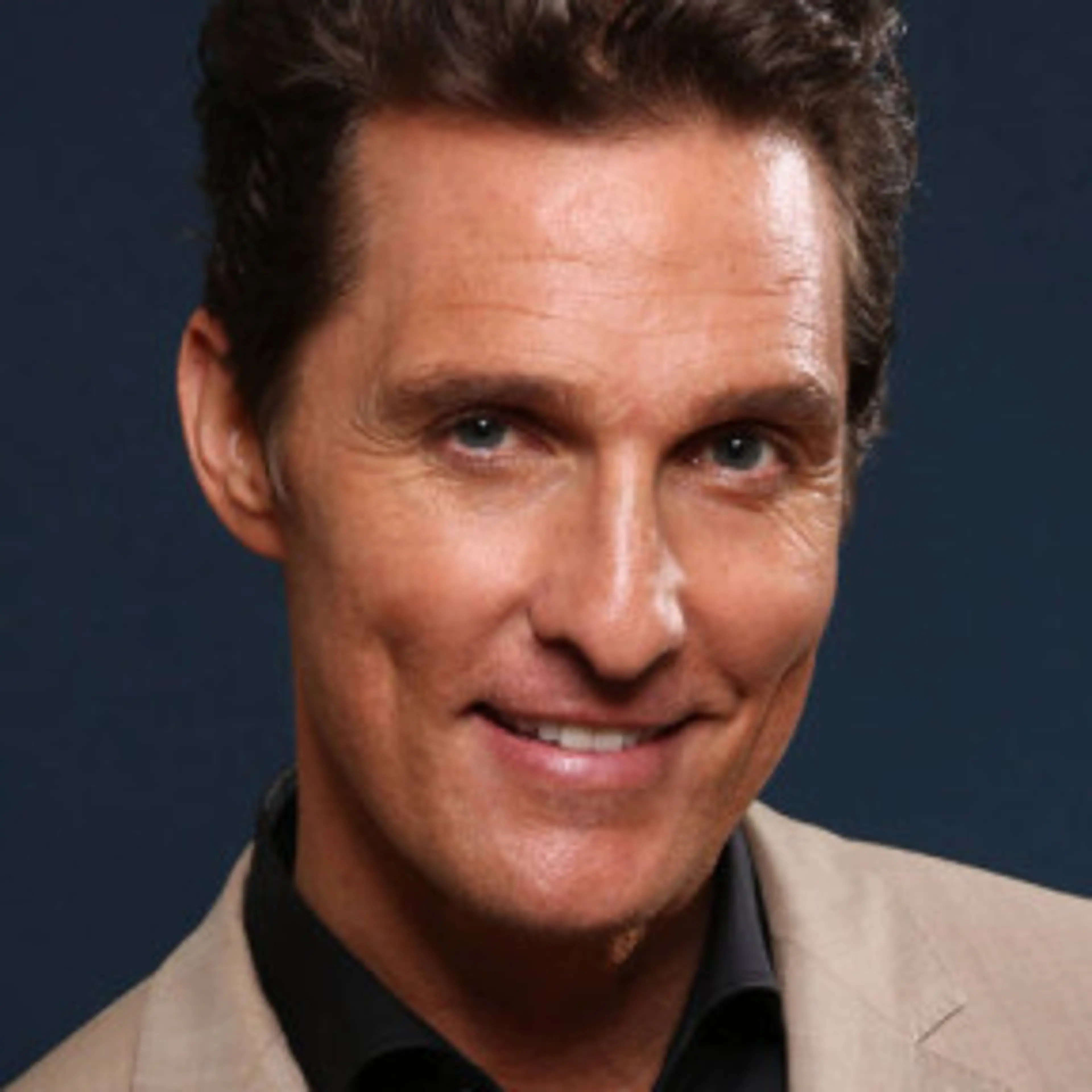Portrait of Matthew McConaughey in a tan jacket and black shirt.