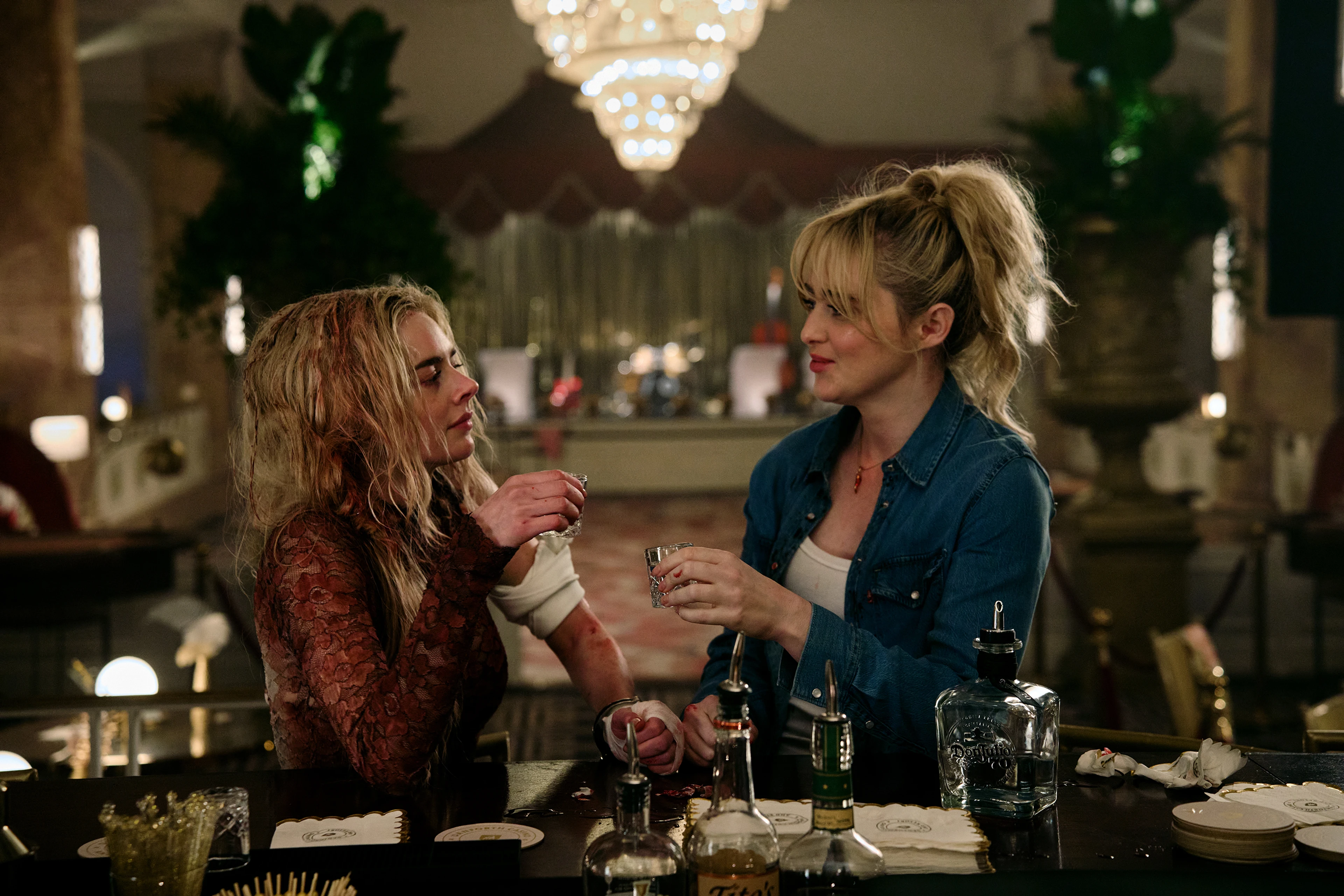 Grace and Faith hold small glasses while standing handcuffed together at a bar.