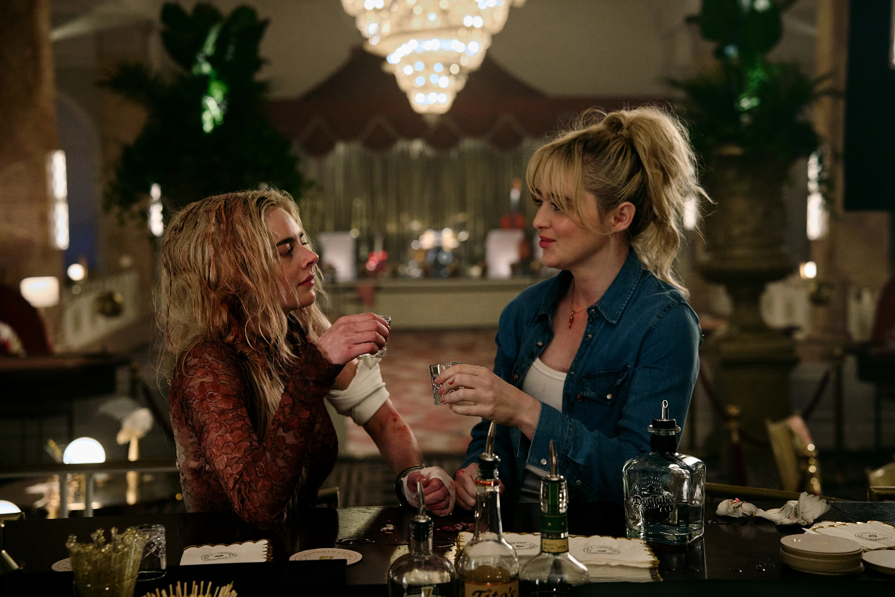 Grace and Faith hold small glasses while standing handcuffed together at a bar.
