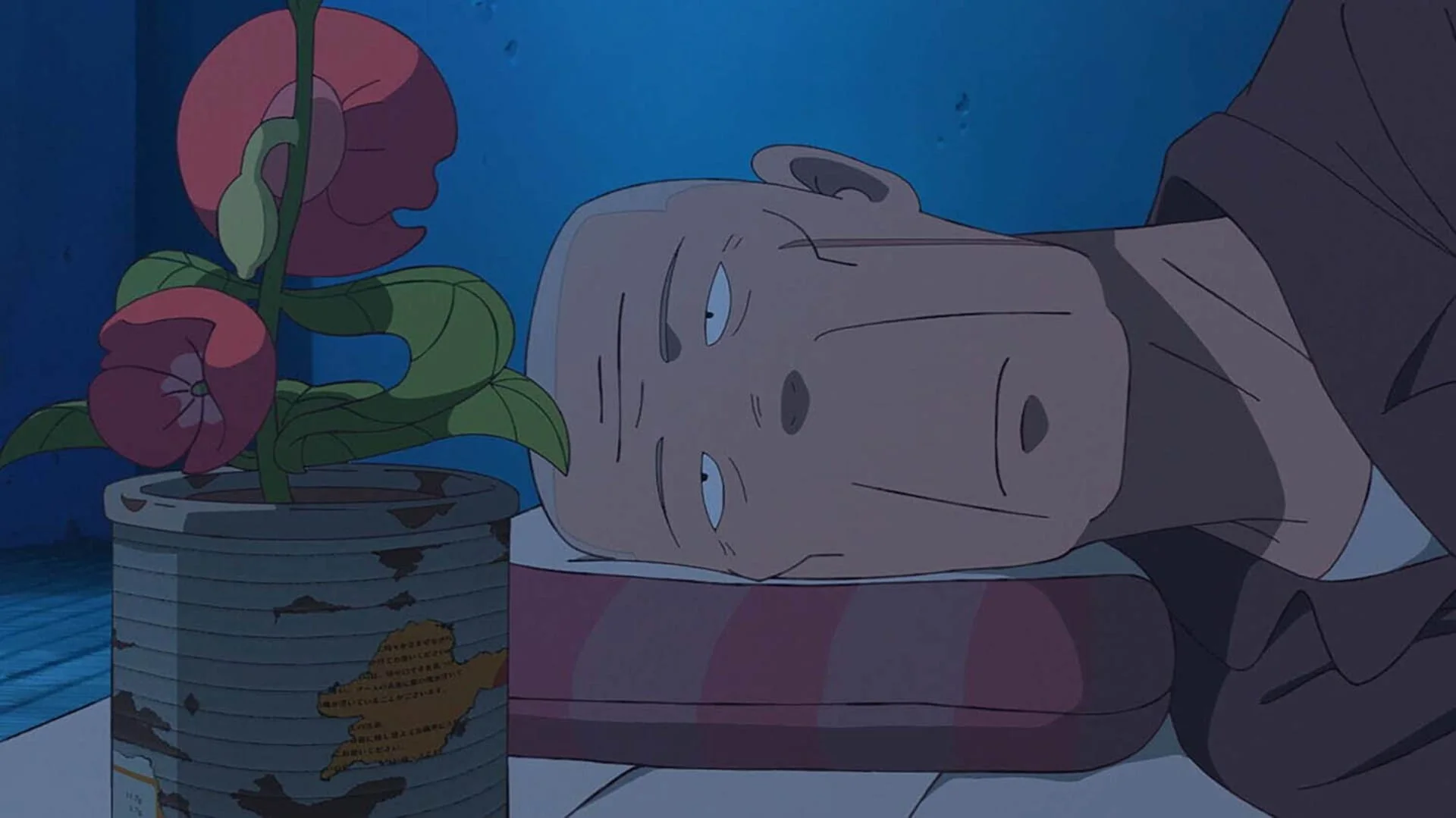 Elderly Akutsu lies beside a can holding a red flower in a blue-lit prison cell.