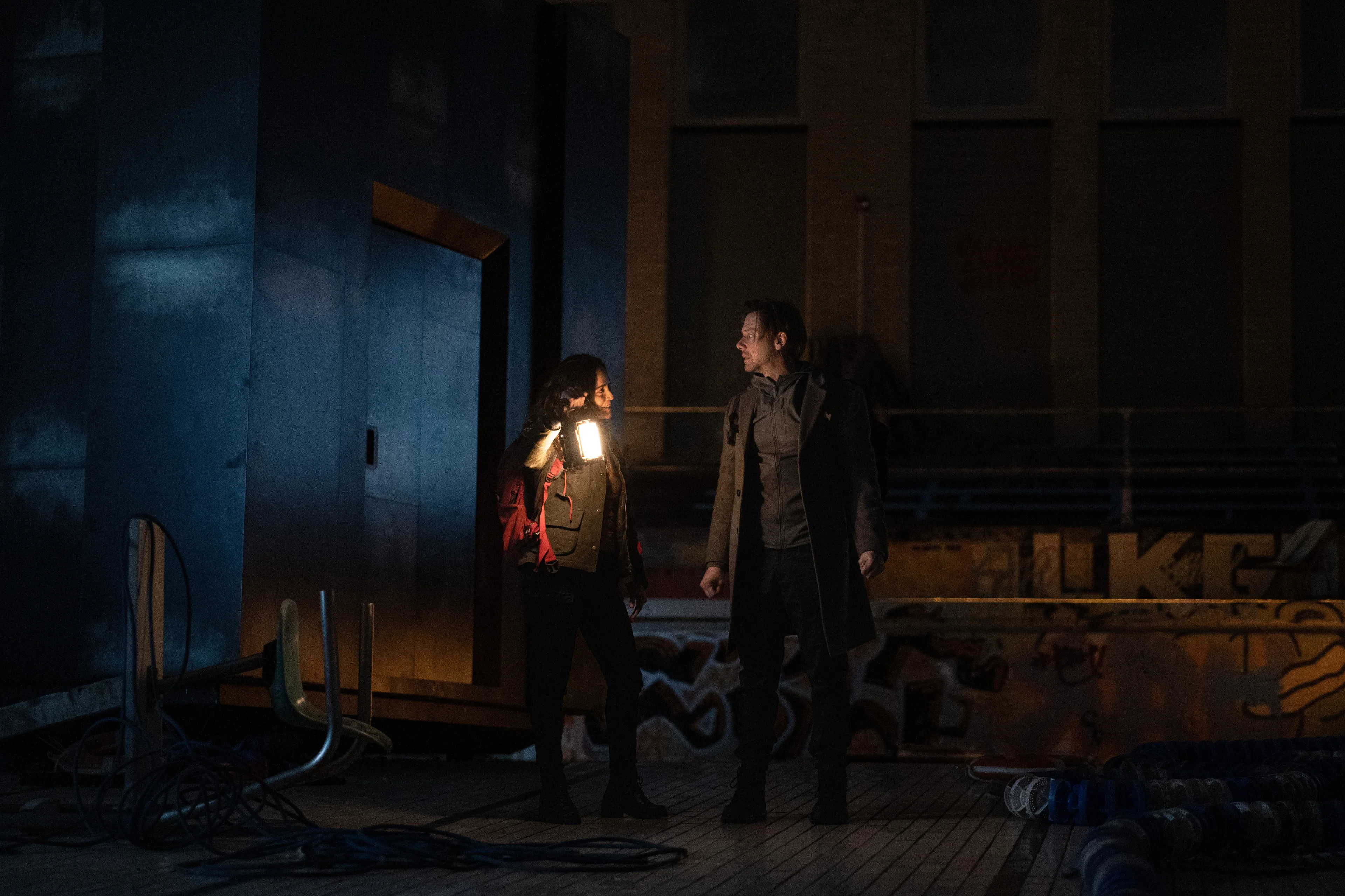 Alice Braga and Jimmi Simpson stand with a lantern in a dark room in Dark Matter Season 2.