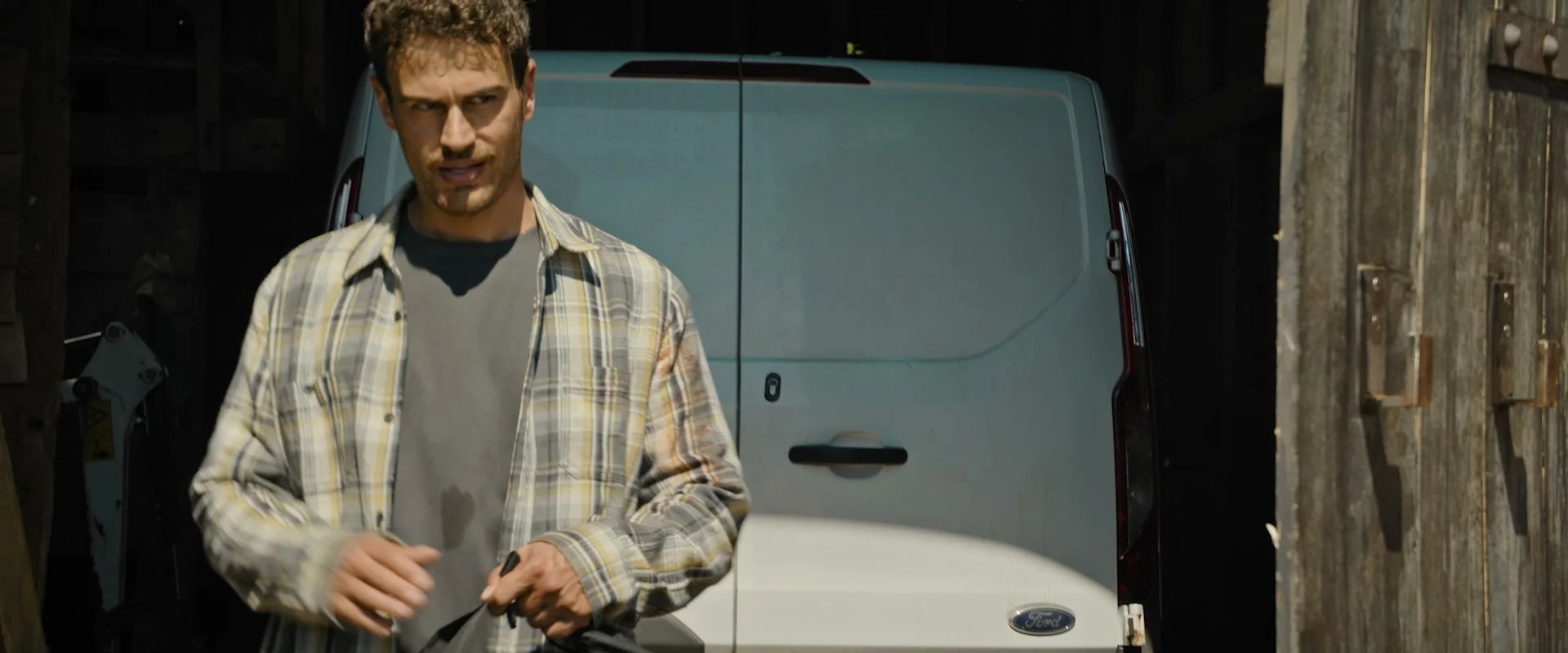 Theo James as Karalis, carrying a bag beside a van.