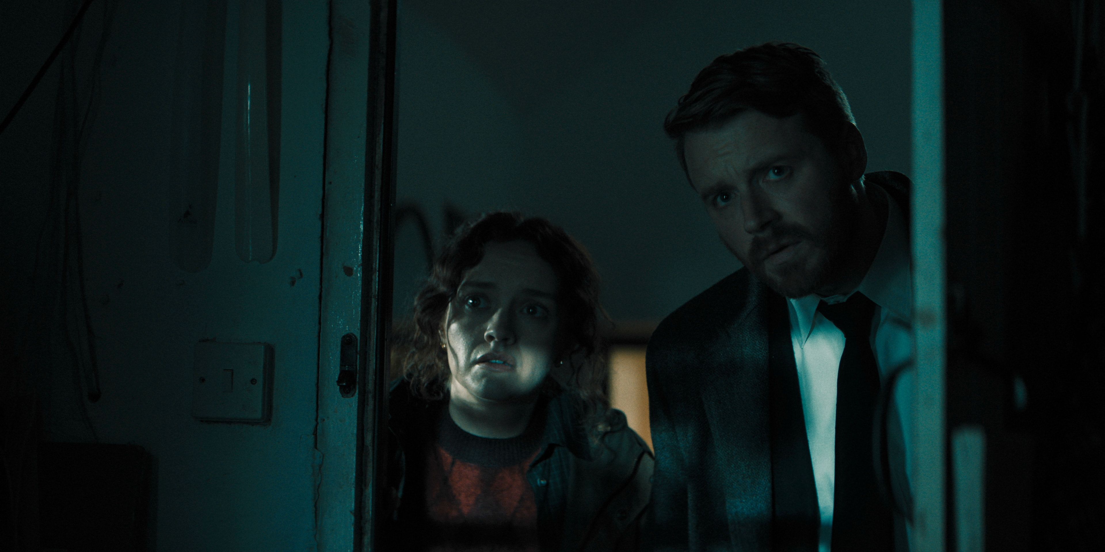 Sid Baker and River Cartwright peer through a doorway together.