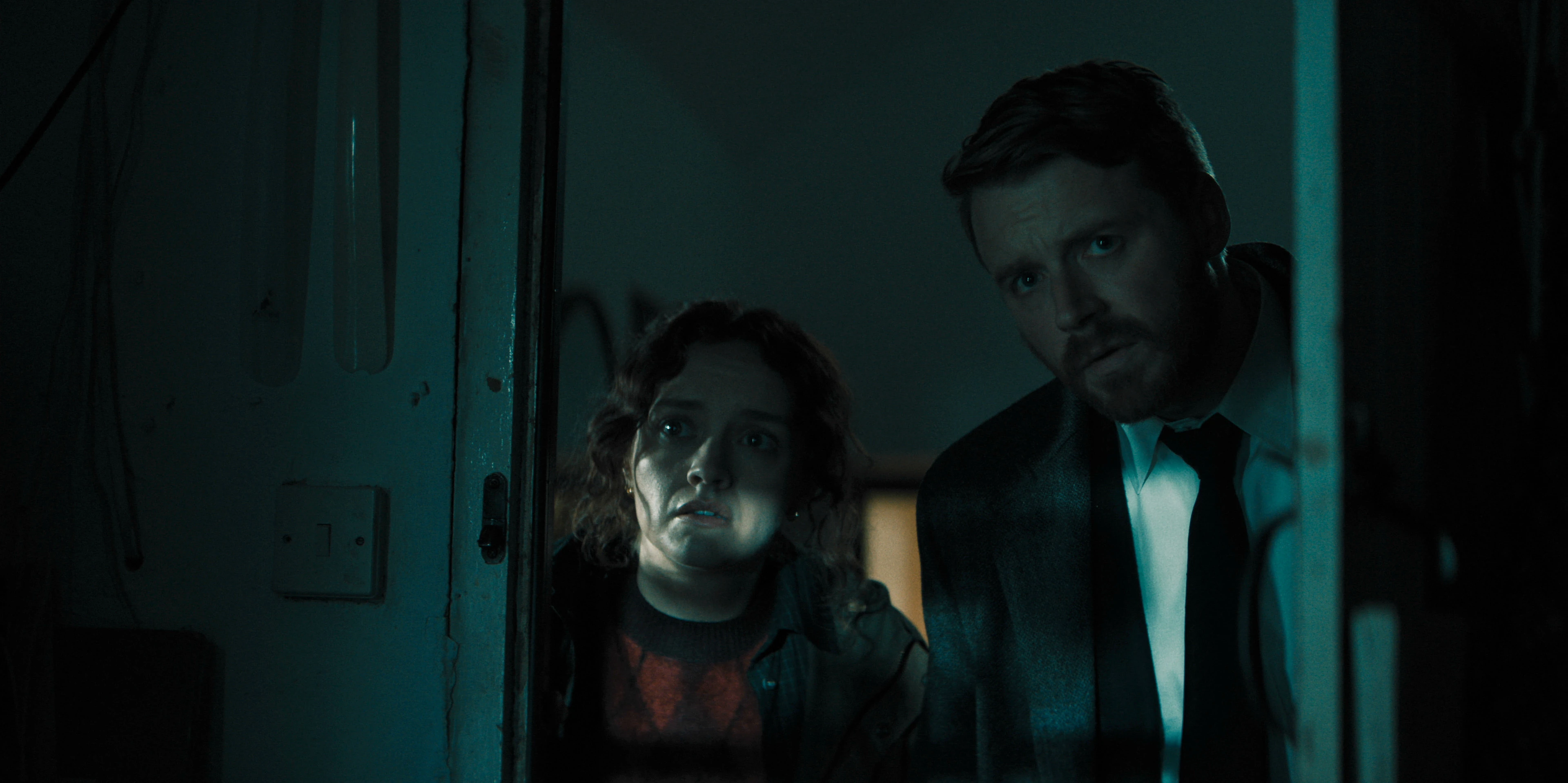 Sid Baker and River Cartwright peer through a doorway together.