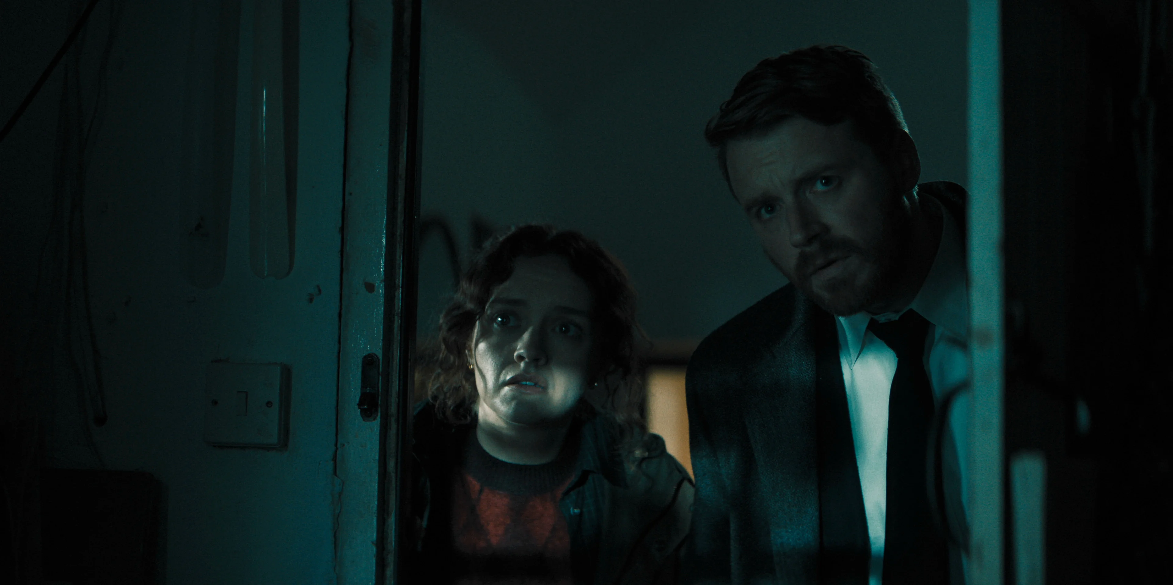 Sid Baker and River Cartwright peer through a doorway together.