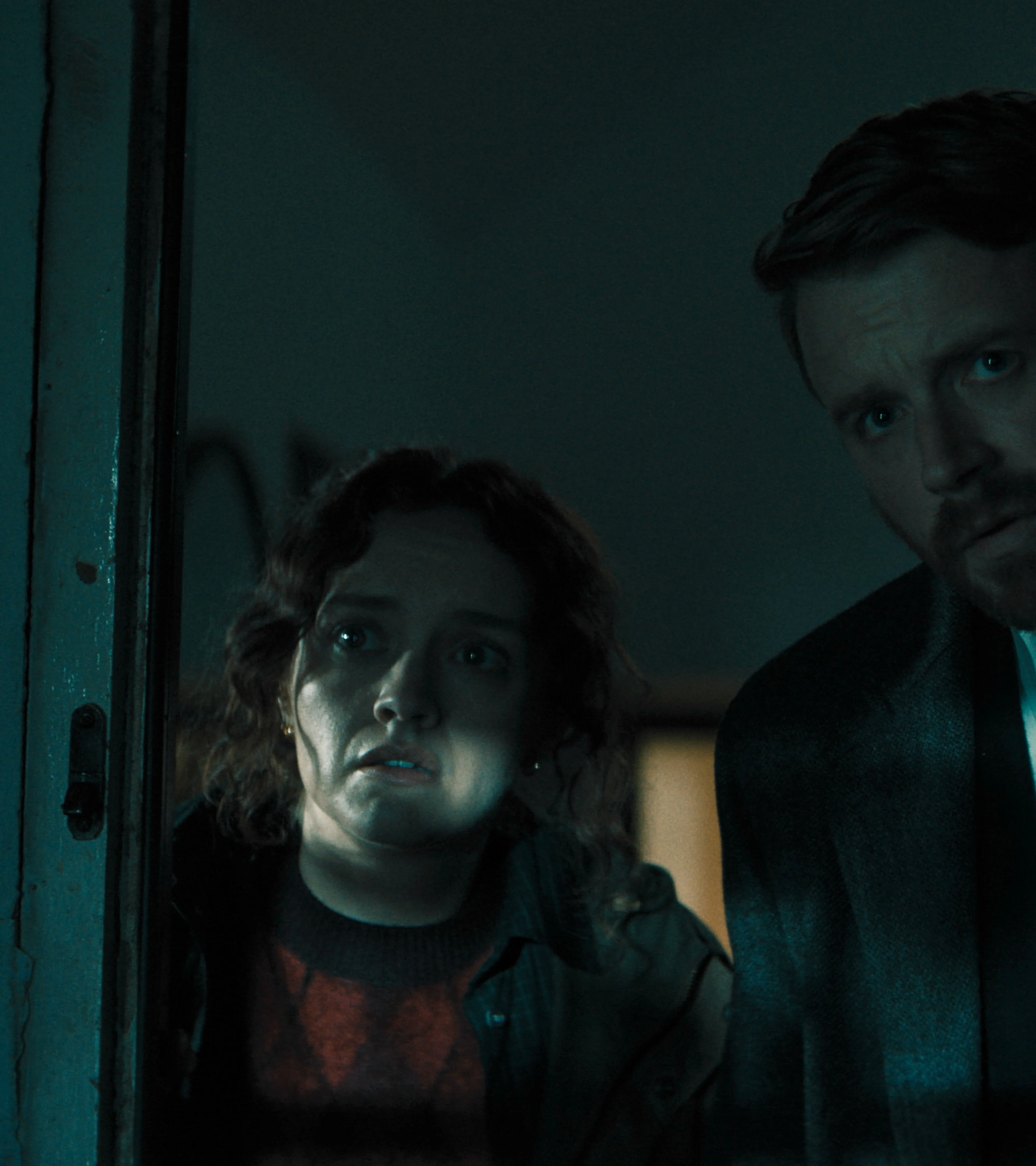 Sid Baker and River Cartwright peer through a doorway together.