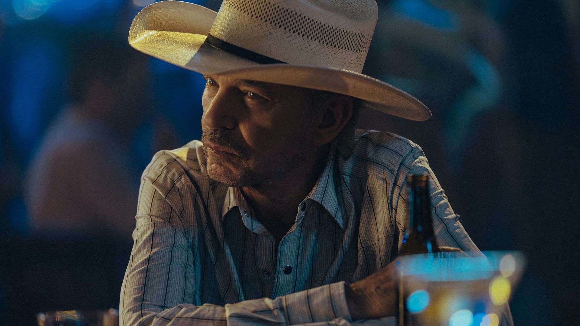 Billy Bob Thornton as Tommy Norris sits at a table at night in Landman.