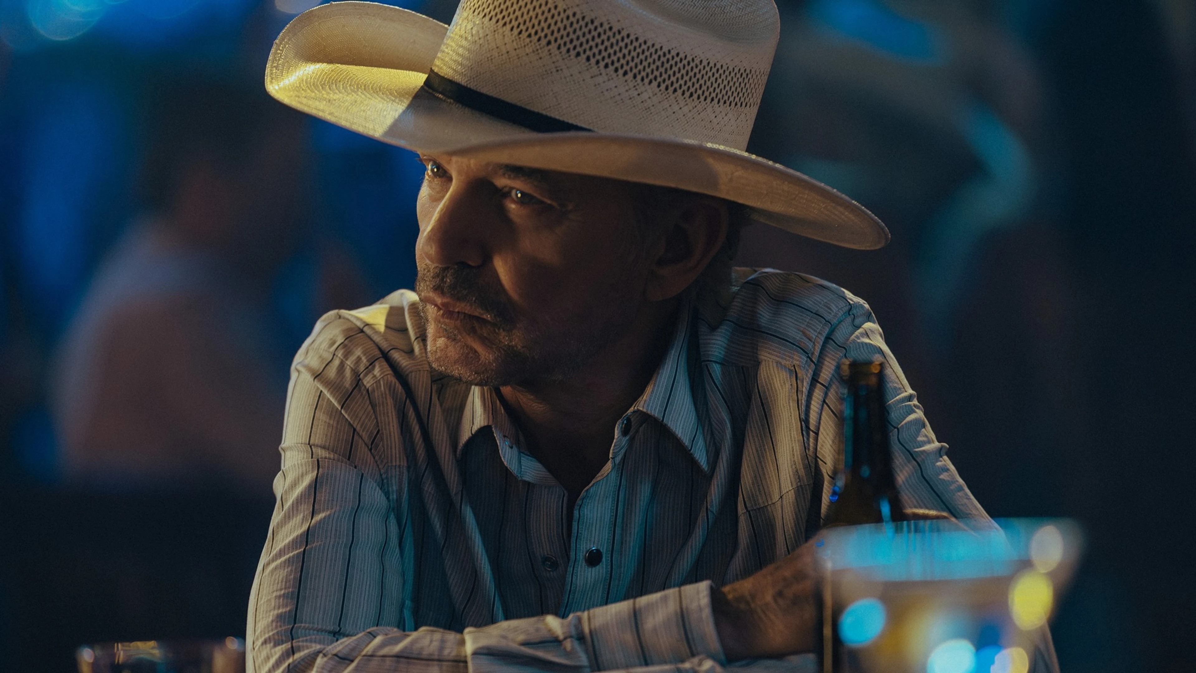Billy Bob Thornton as Tommy Norris sits at a table at night in Landman.
