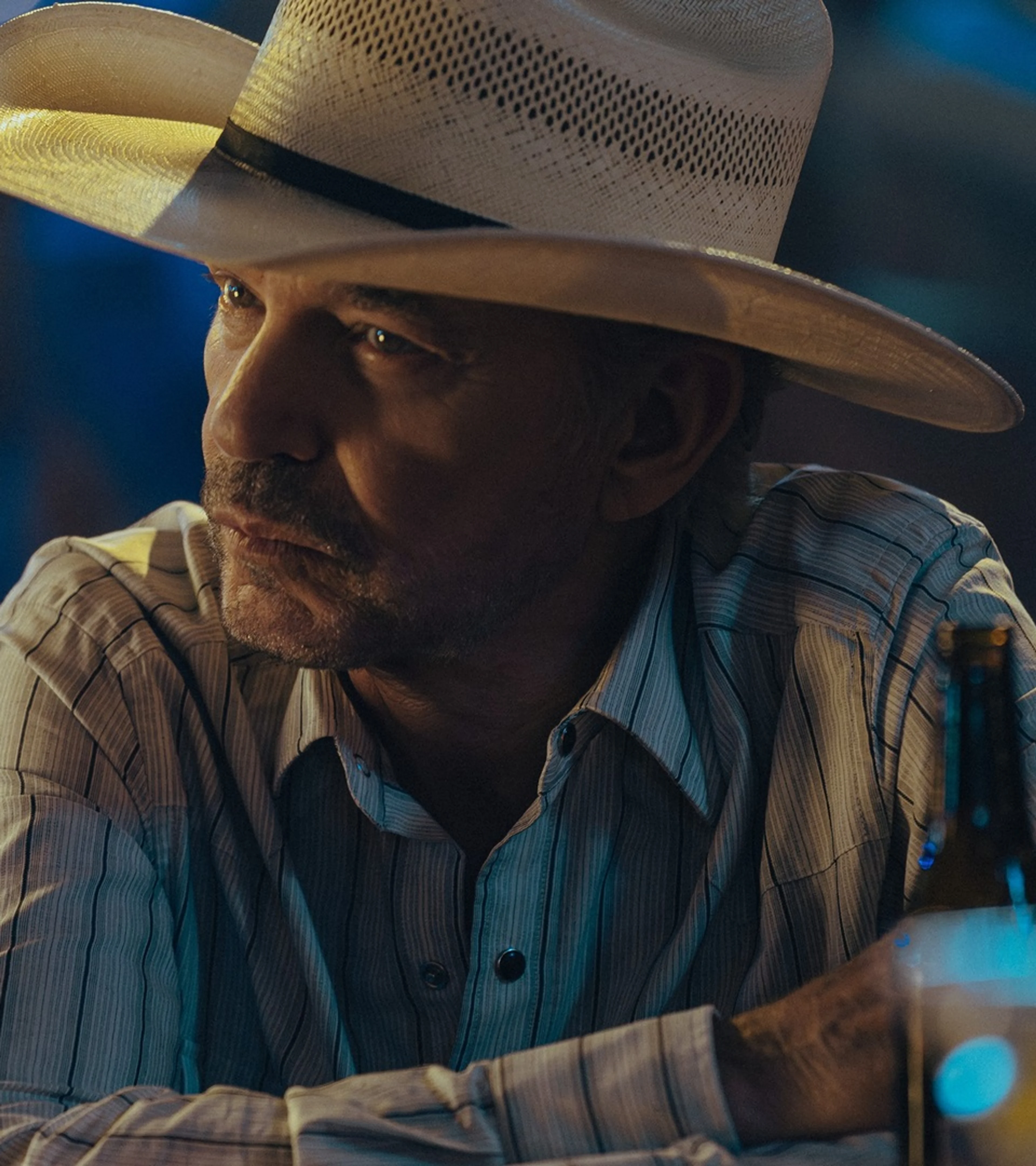 Billy Bob Thornton as Tommy Norris sits at a table at night in Landman.