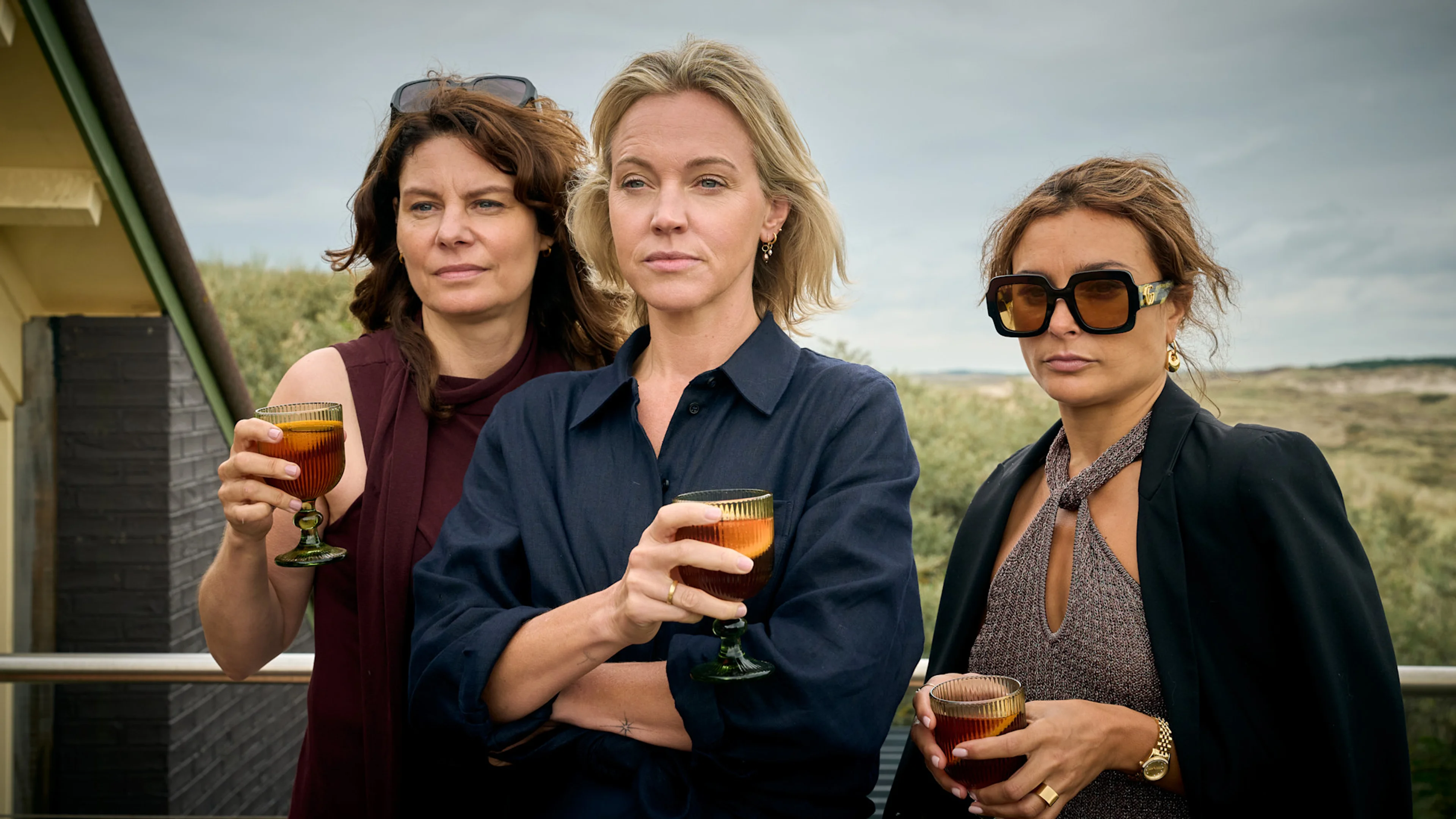 Three women from the dinner club hold drinks at a coastal house in The Perfect Lie.