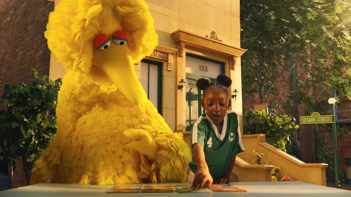 Big Bird and a child playing at a table on Sesame Street.