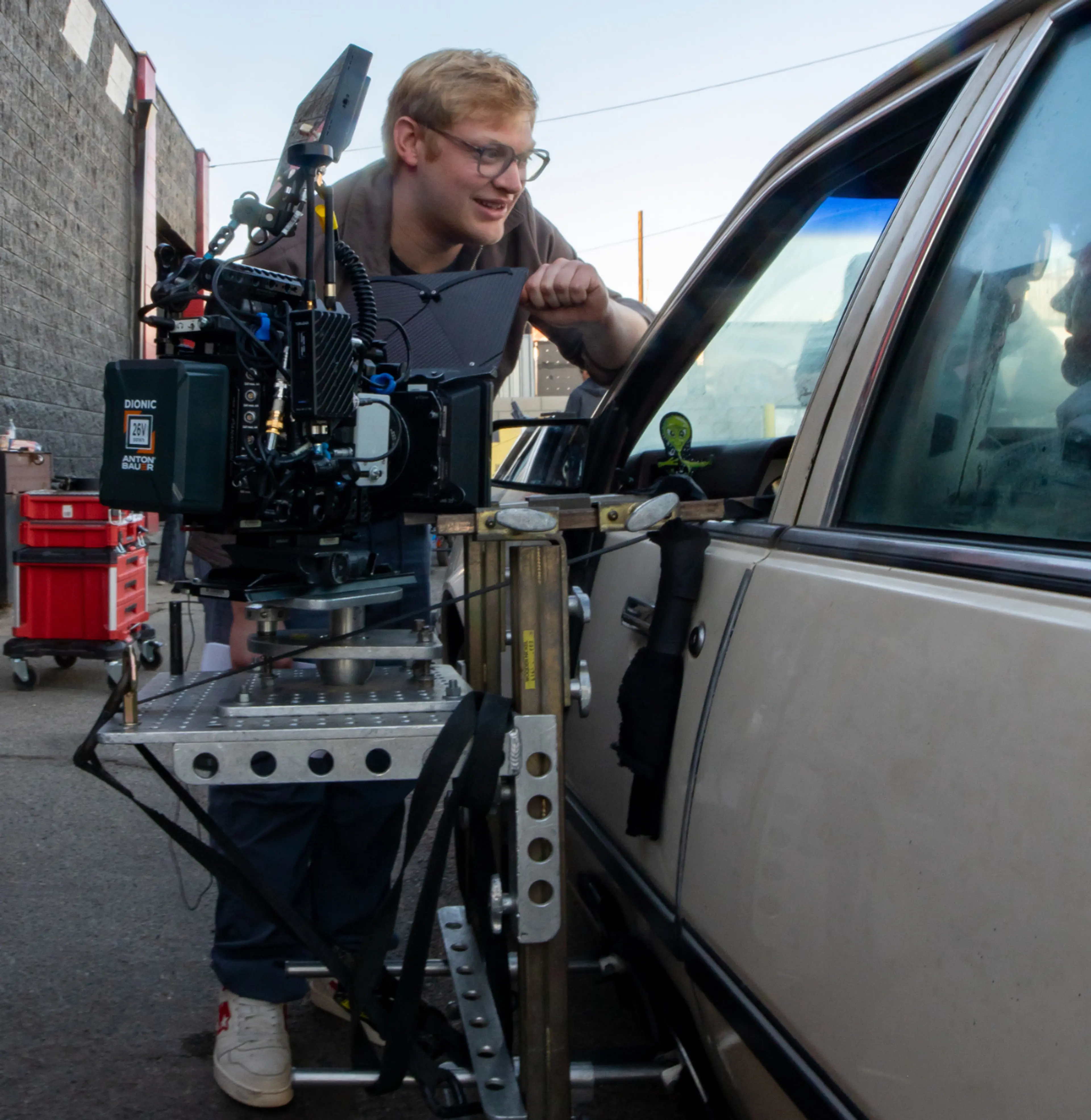 Director Curry Barker works beside a camera outside a car.