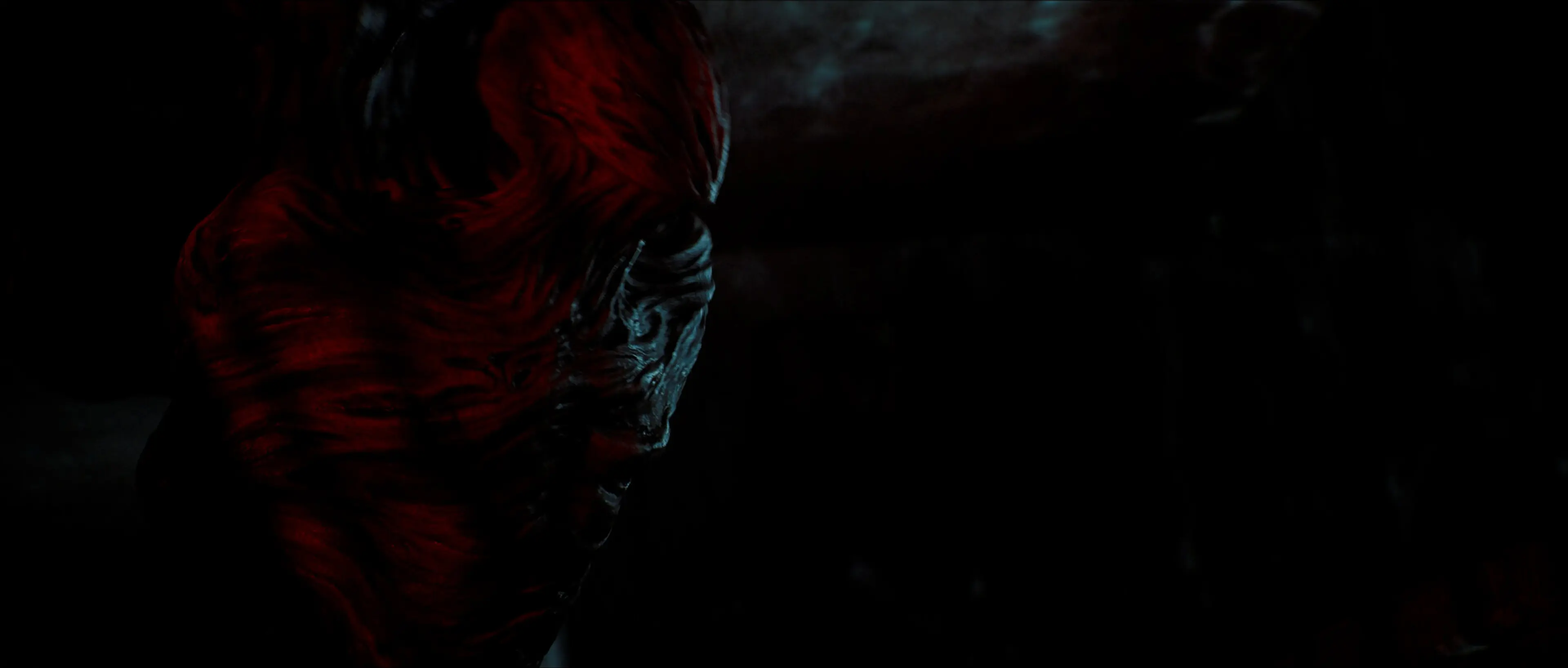 A distorted creature is shown close up in red and black lighting.