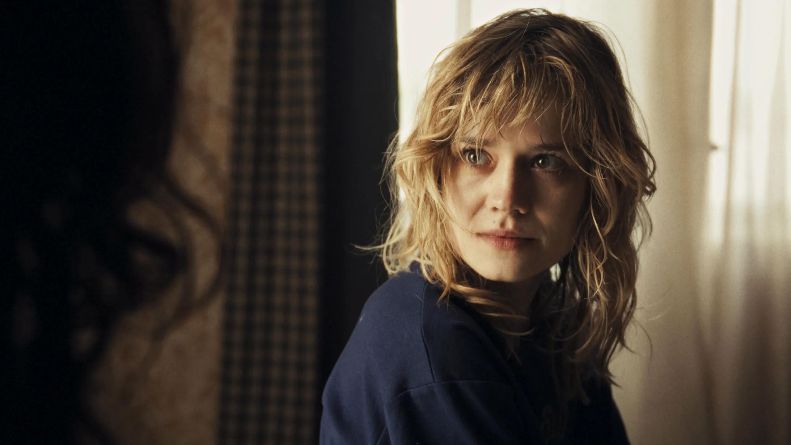 Phoebe turns toward someone beside a bright window in City of Blood.