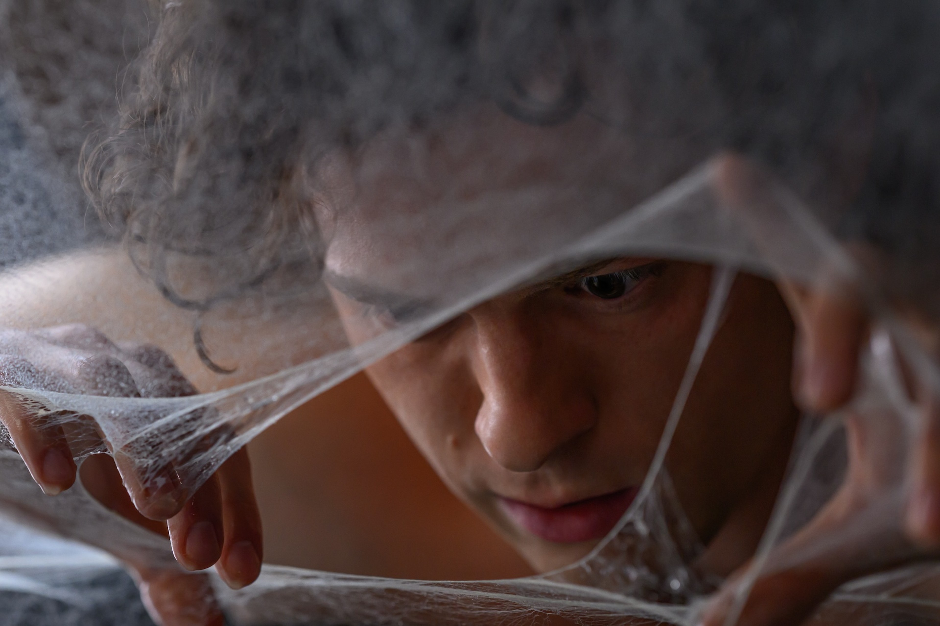 Tom Holland as Peter Parker looks through webbing in Spider-Man: Brand New Day.