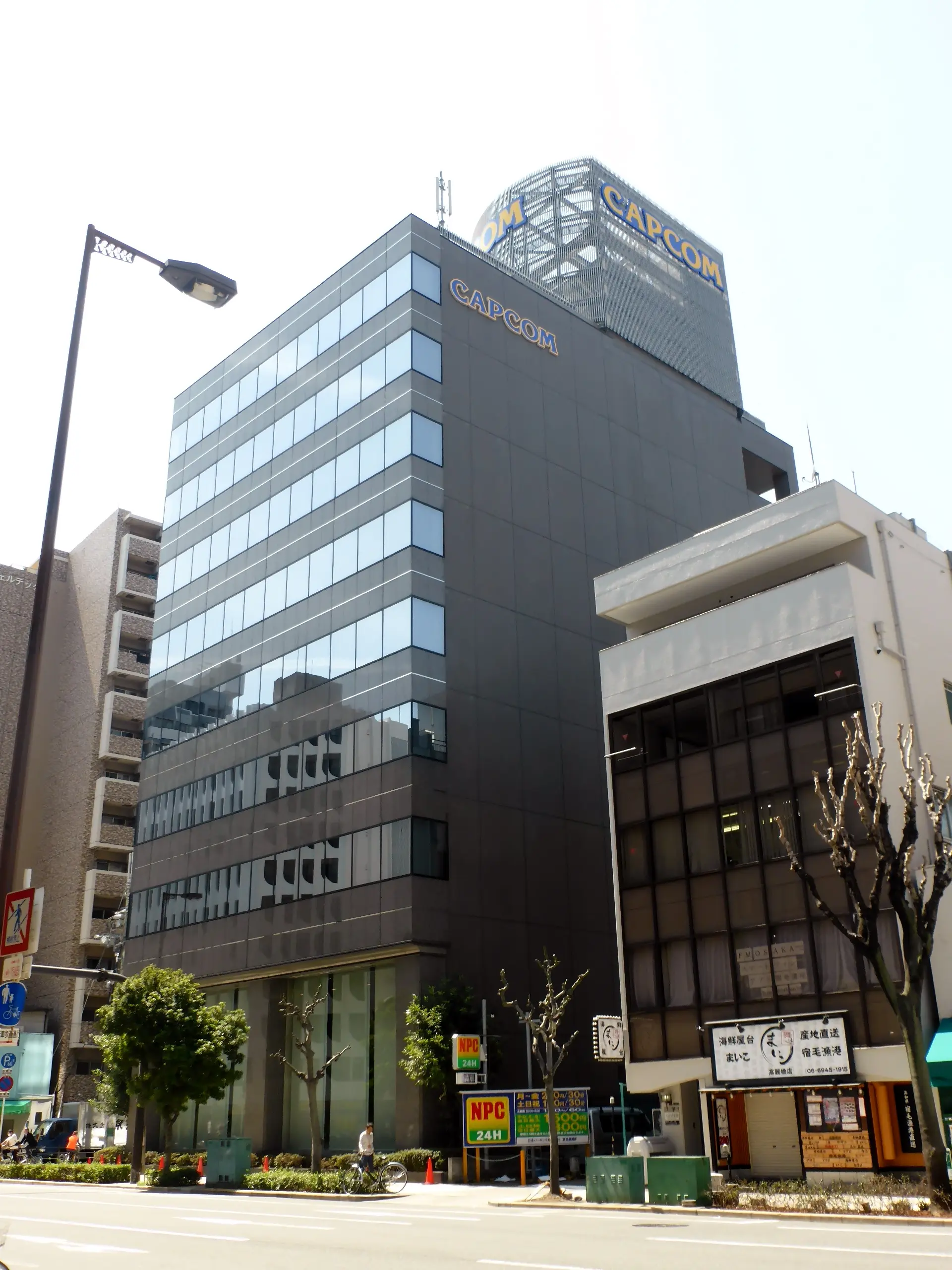 Capcom’s Osaka headquarters, with blue-and-yellow CAPCOM signs above its glass facade.