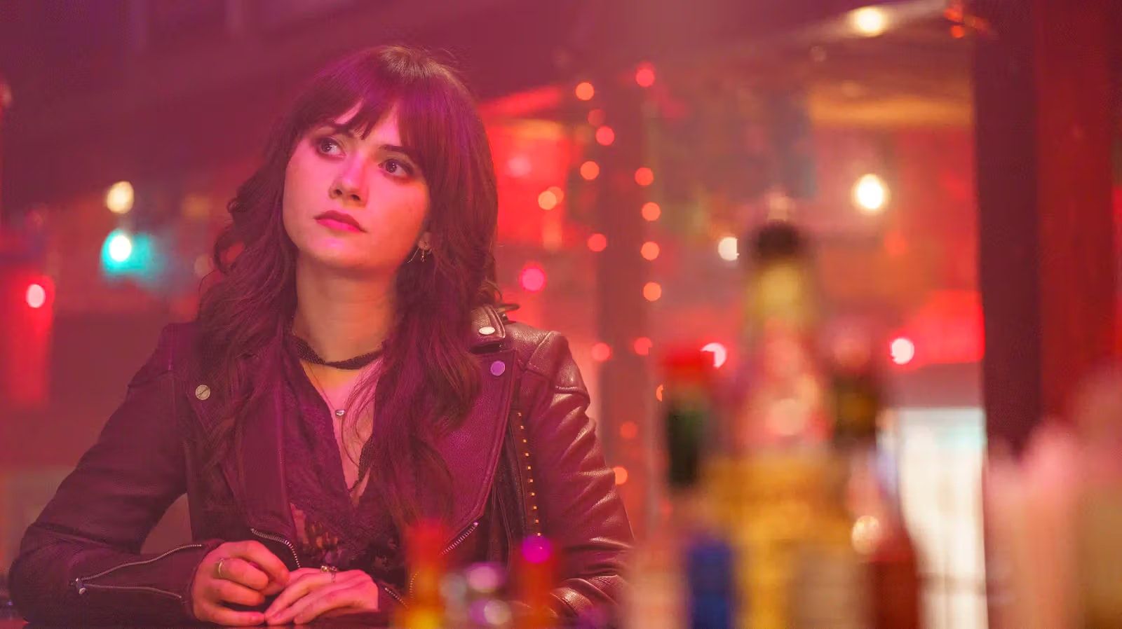 Emilia Jones as Harper sits at a bar under warm red lights.