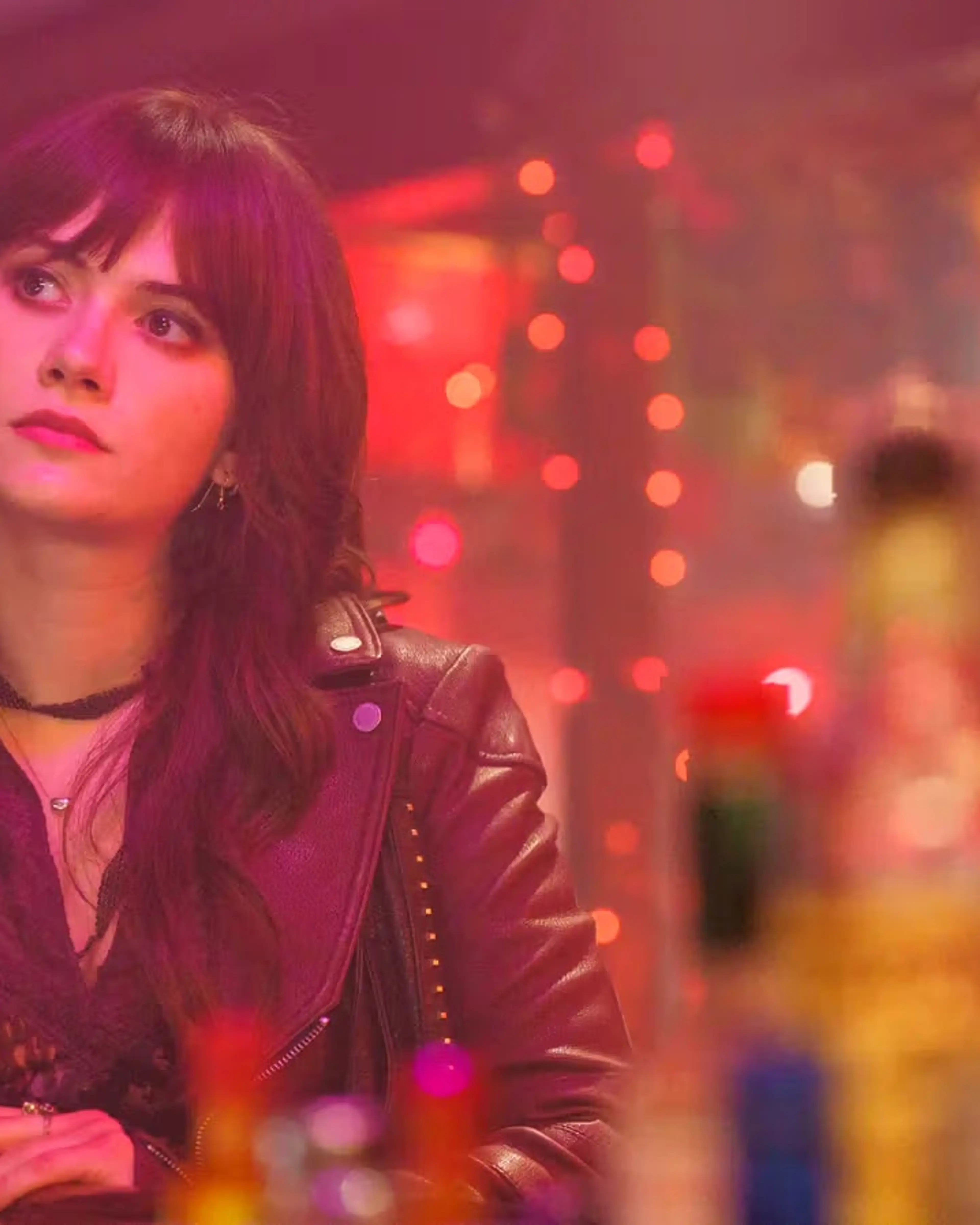Emilia Jones as Harper sits at a bar under warm red lights.