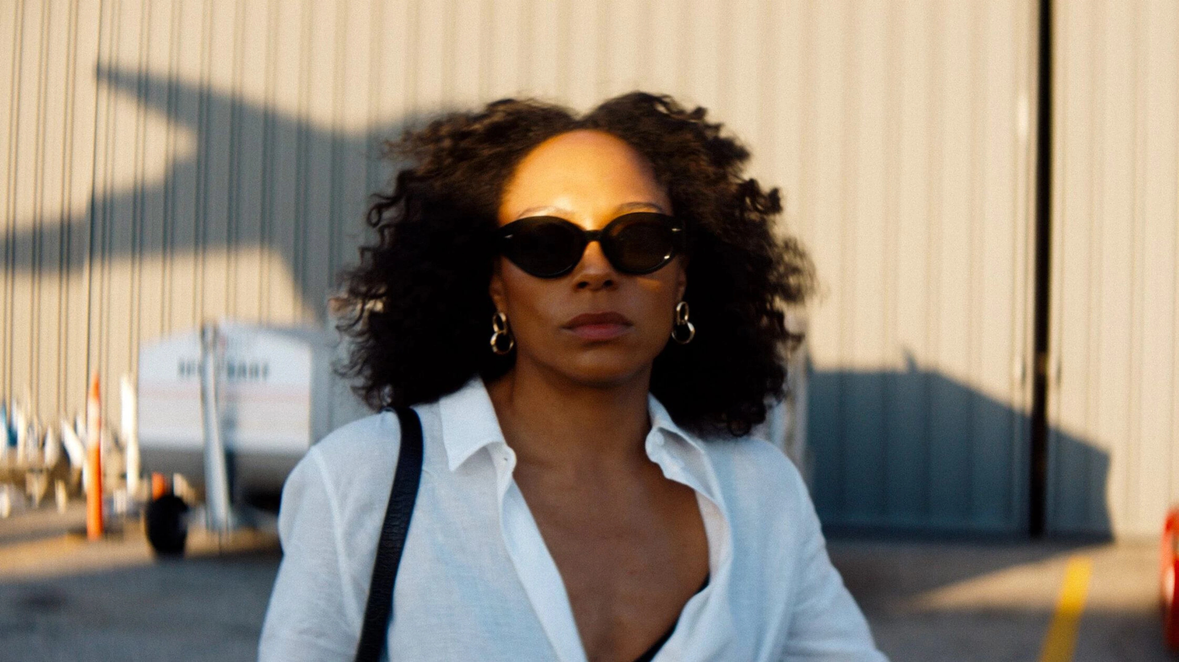 Rosalind Eleazar as Misty Green walks outside wearing sunglasses and a white shirt.