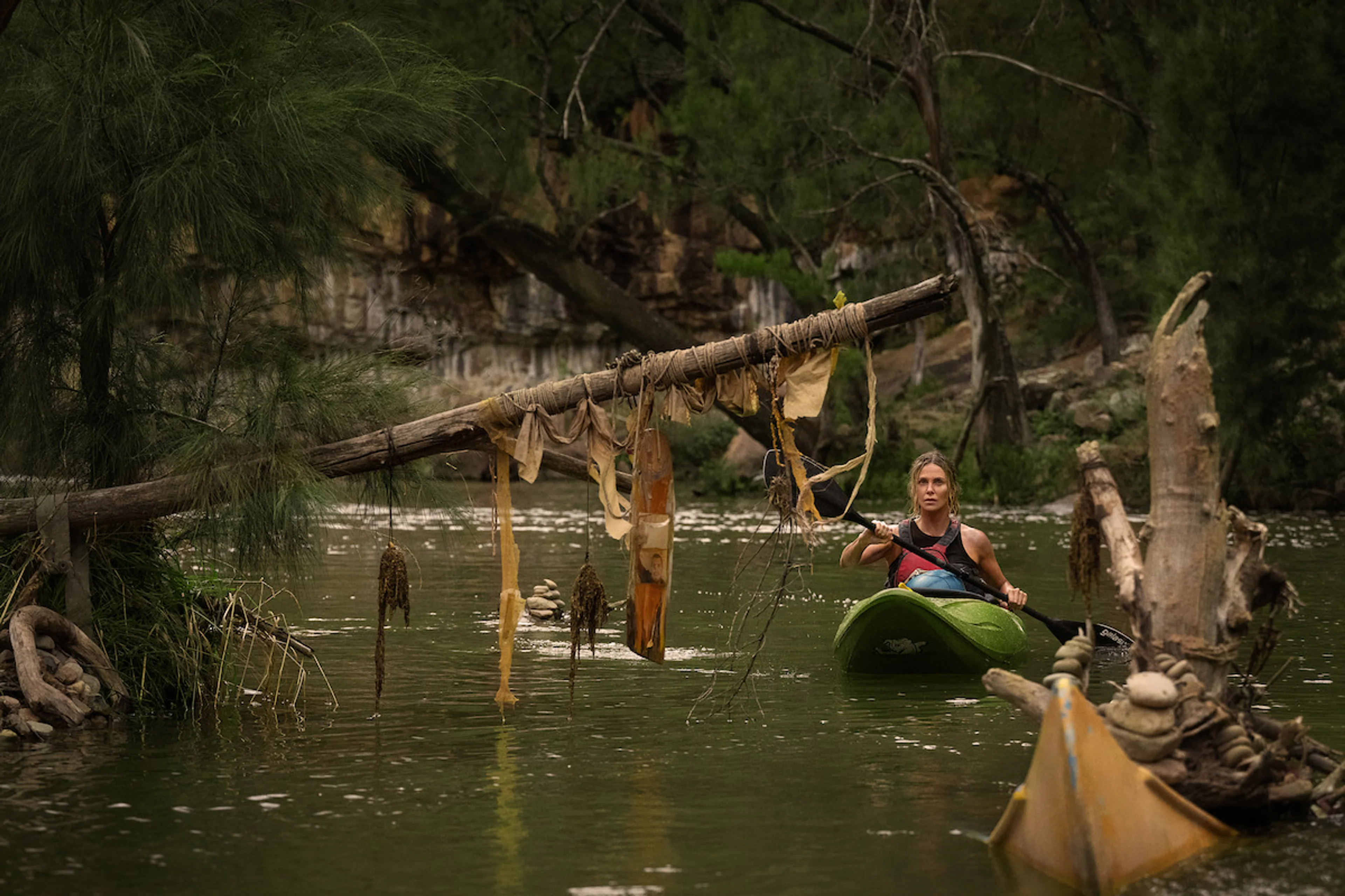 Sasha paddles a green kayak past a fallen tree on a forest river.