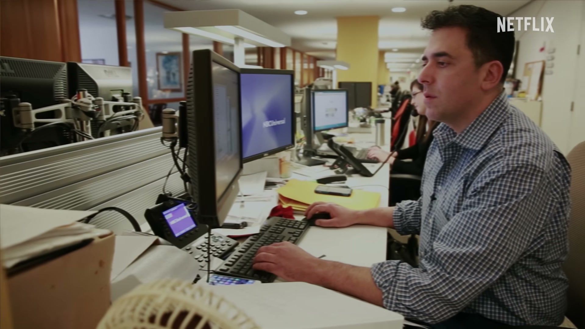 A journalist works at a computer in a newsroom scene from The Widower: ’Til Death Do Us Part.