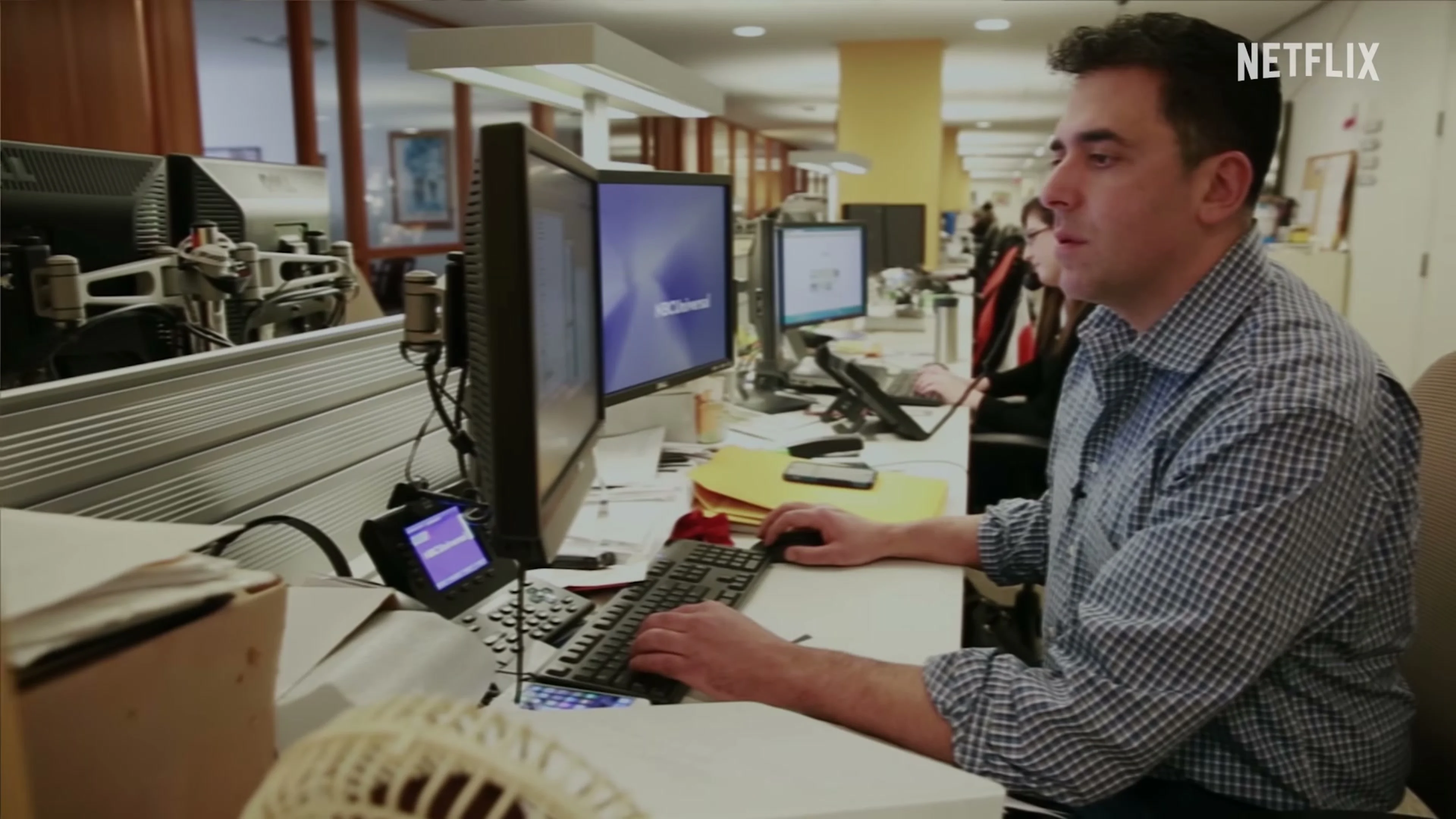 A journalist works at a computer in a newsroom scene from The Widower: ’Til Death Do Us Part.