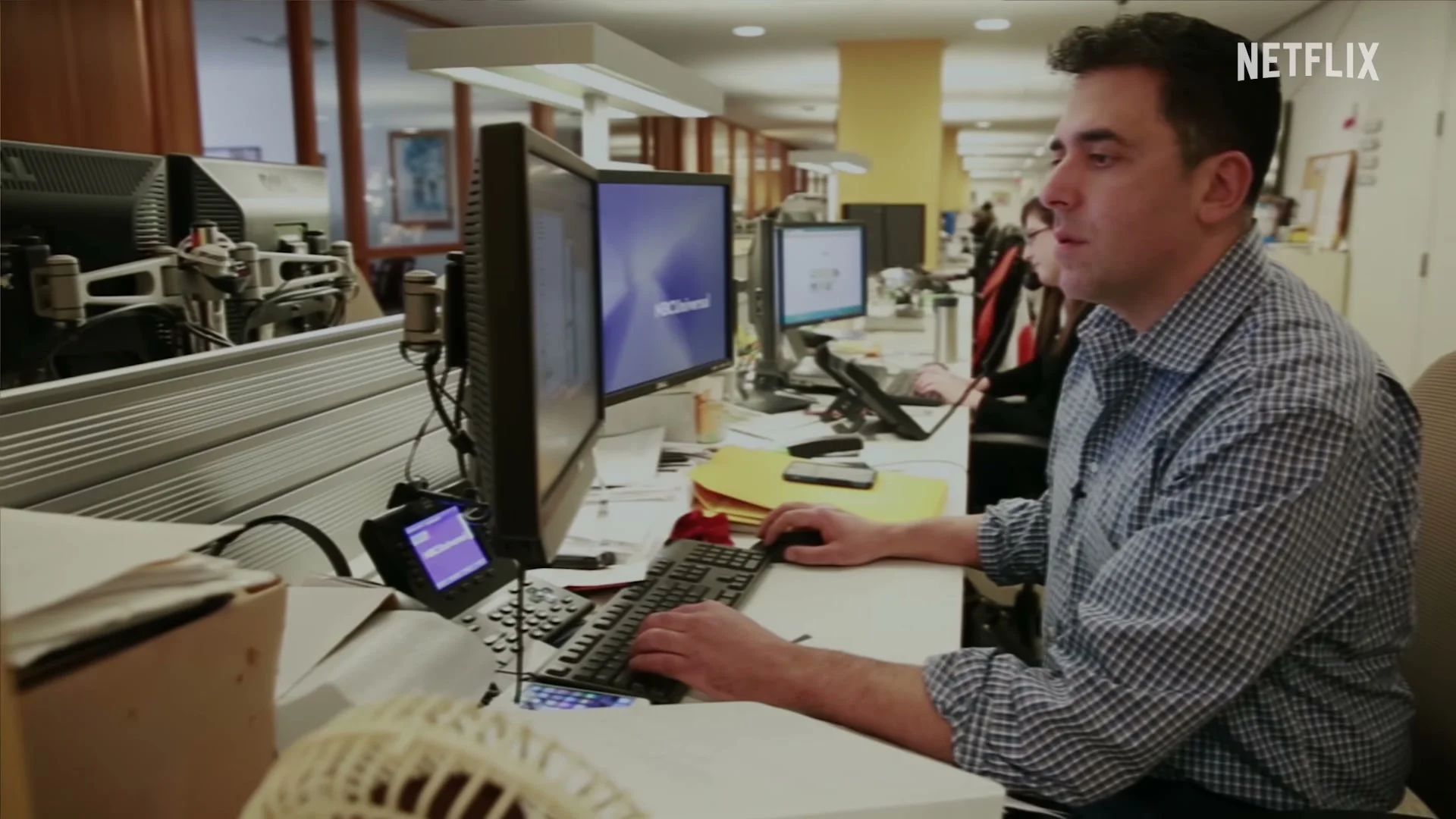 A journalist works at a computer in a newsroom scene from The Widower: ’Til Death Do Us Part.